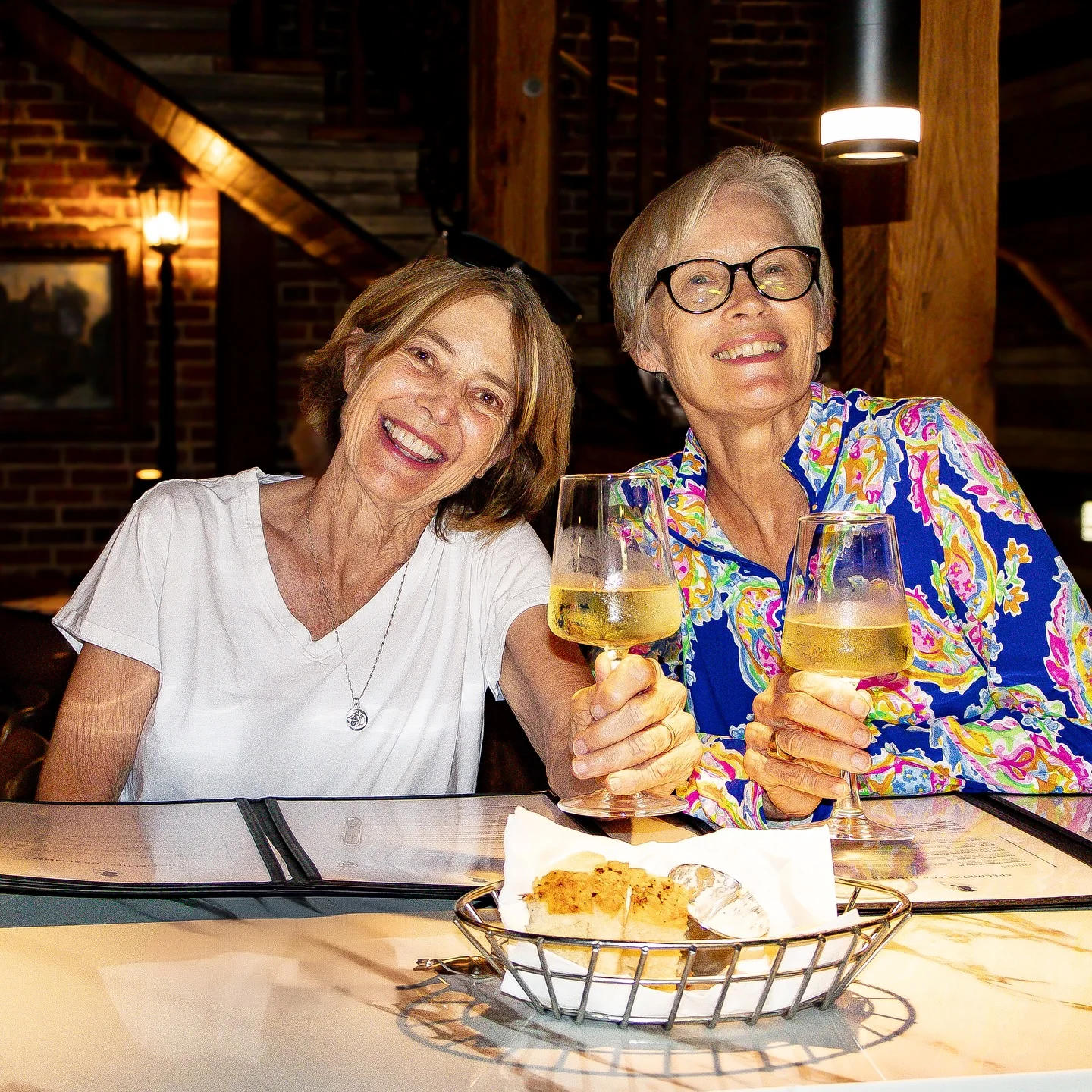 Two women toasting with drinks in a cozy restaurant setting