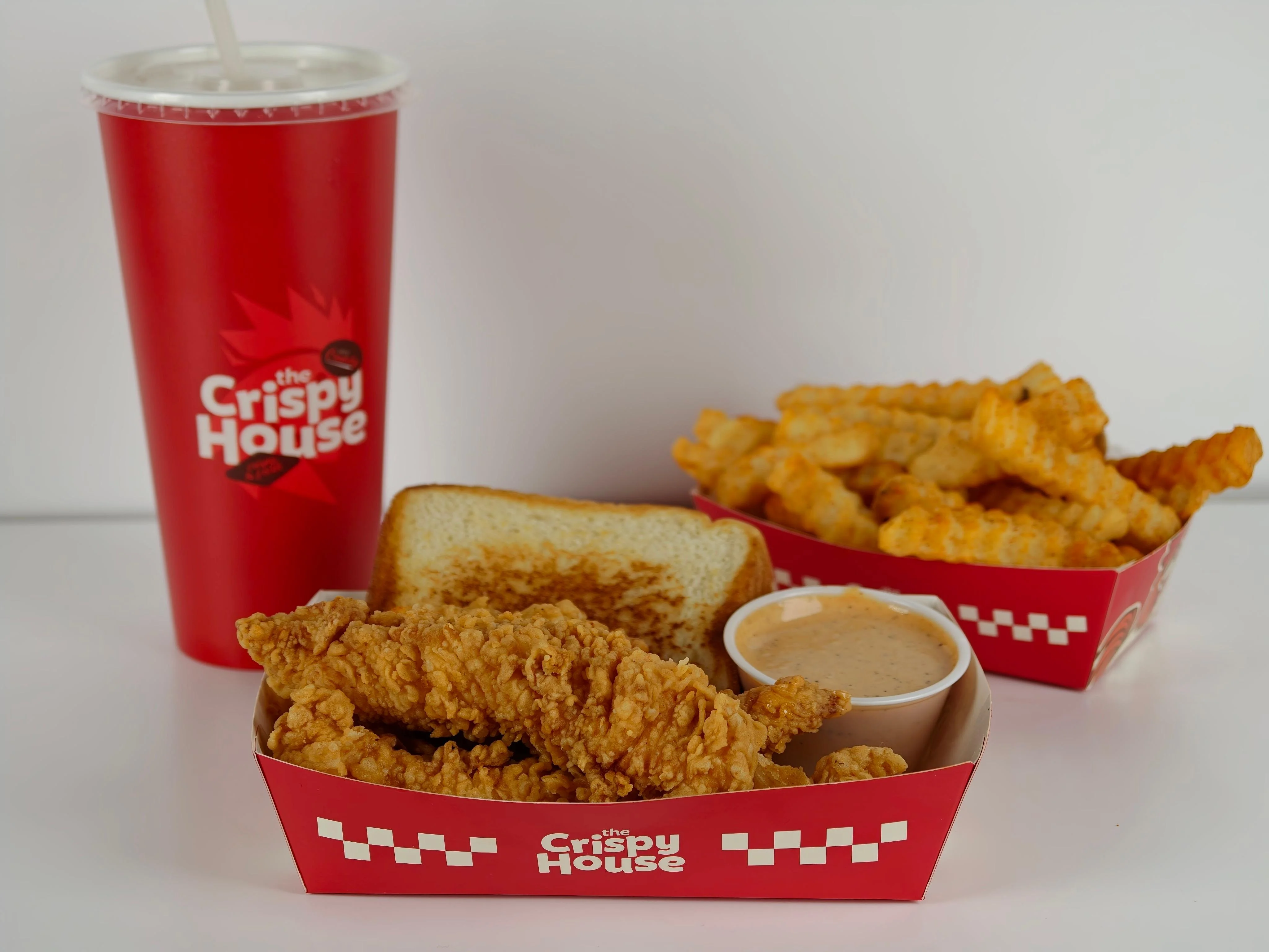 A serving of fried chicken tenders, toast, a dipping sauce, and crinkle-cut fries in a branded tray.