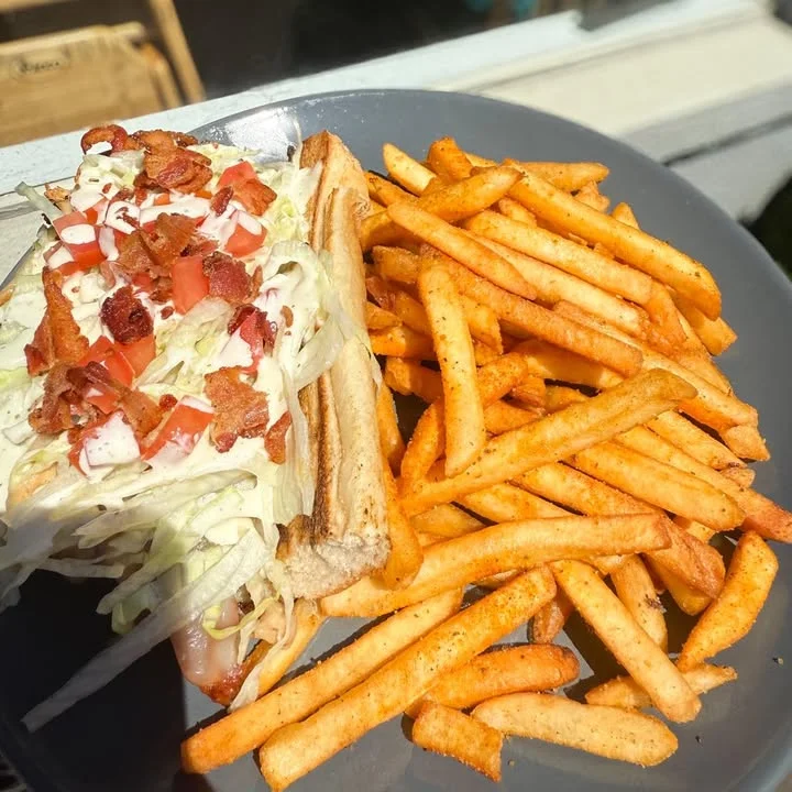 A hearty sandwich topped with lettuce, diced tomatoes, and bacon, served alongside a generous portion of crispy French fries.