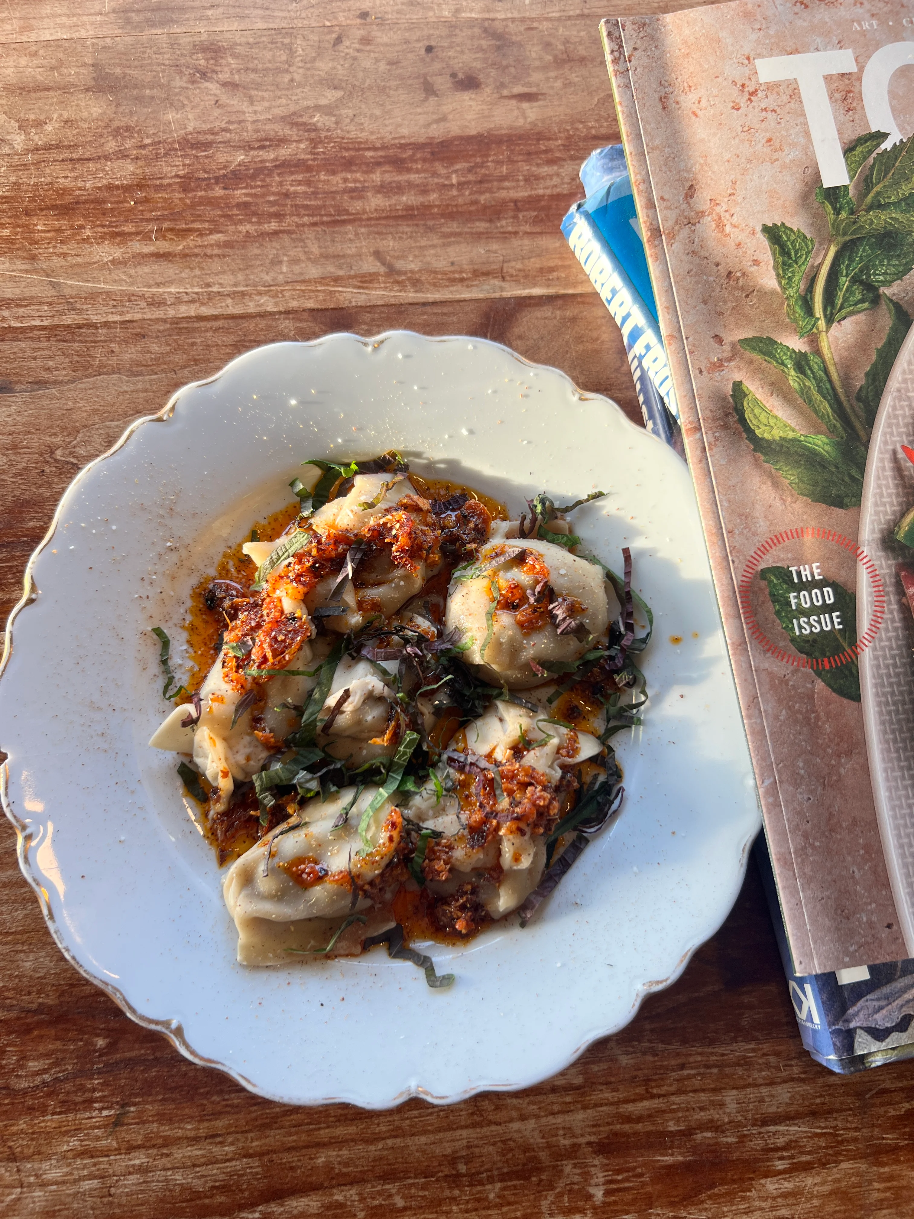 A plate of dumplings drizzled with sauce and garnished with herbs, alongside a food magazine.