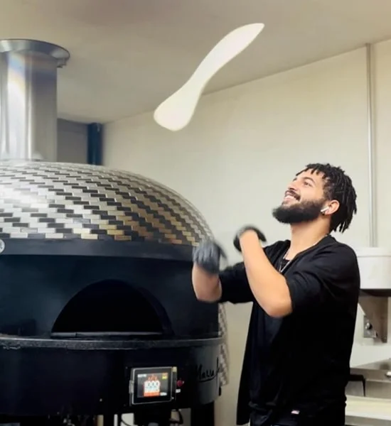 Pizza chef tossing dough in a wood-fired oven