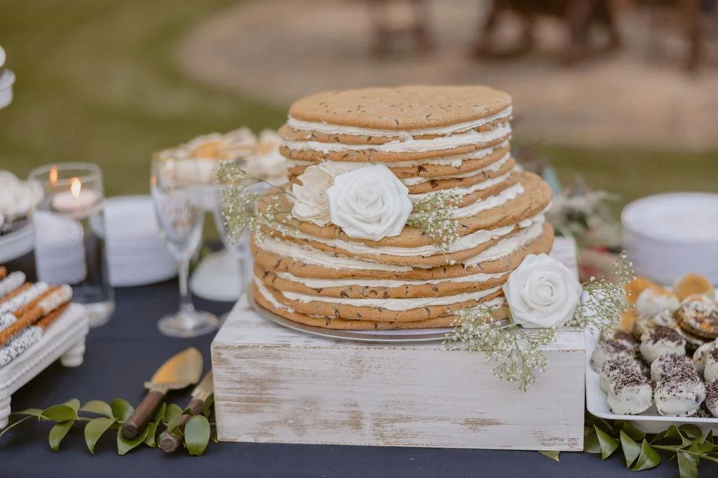 A tiered cookie cake made of large stacked cookies with frosting layers in between, decorated with white roses and baby’s breath.
