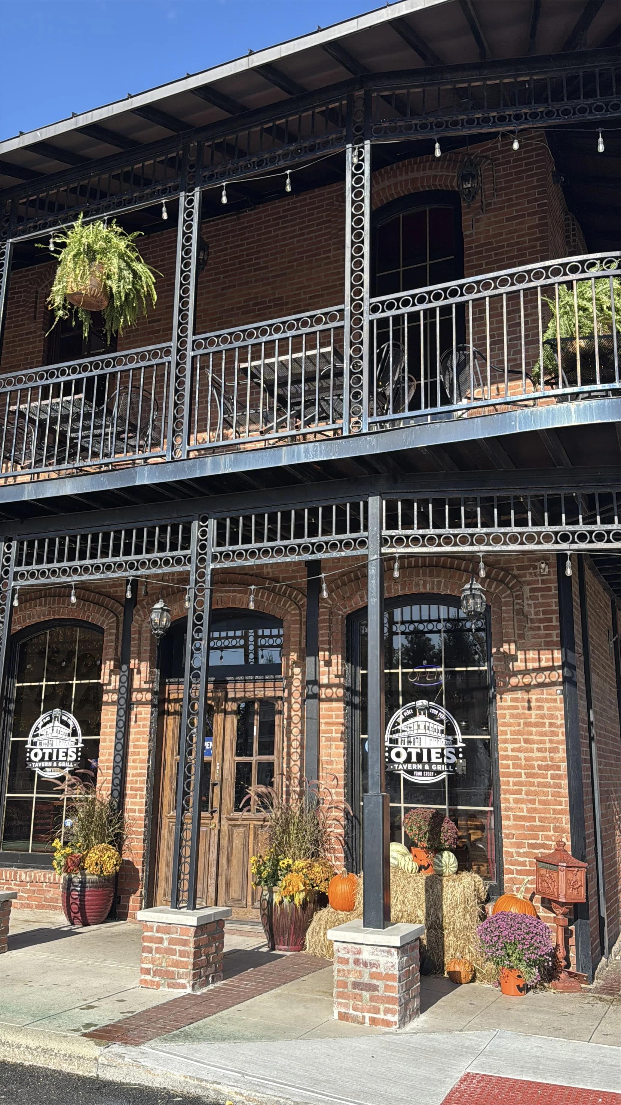 The exterior of a brick building featuring a welcoming entrance with decorative plants and signage. The overhead balcony adds to the charm of the structure.