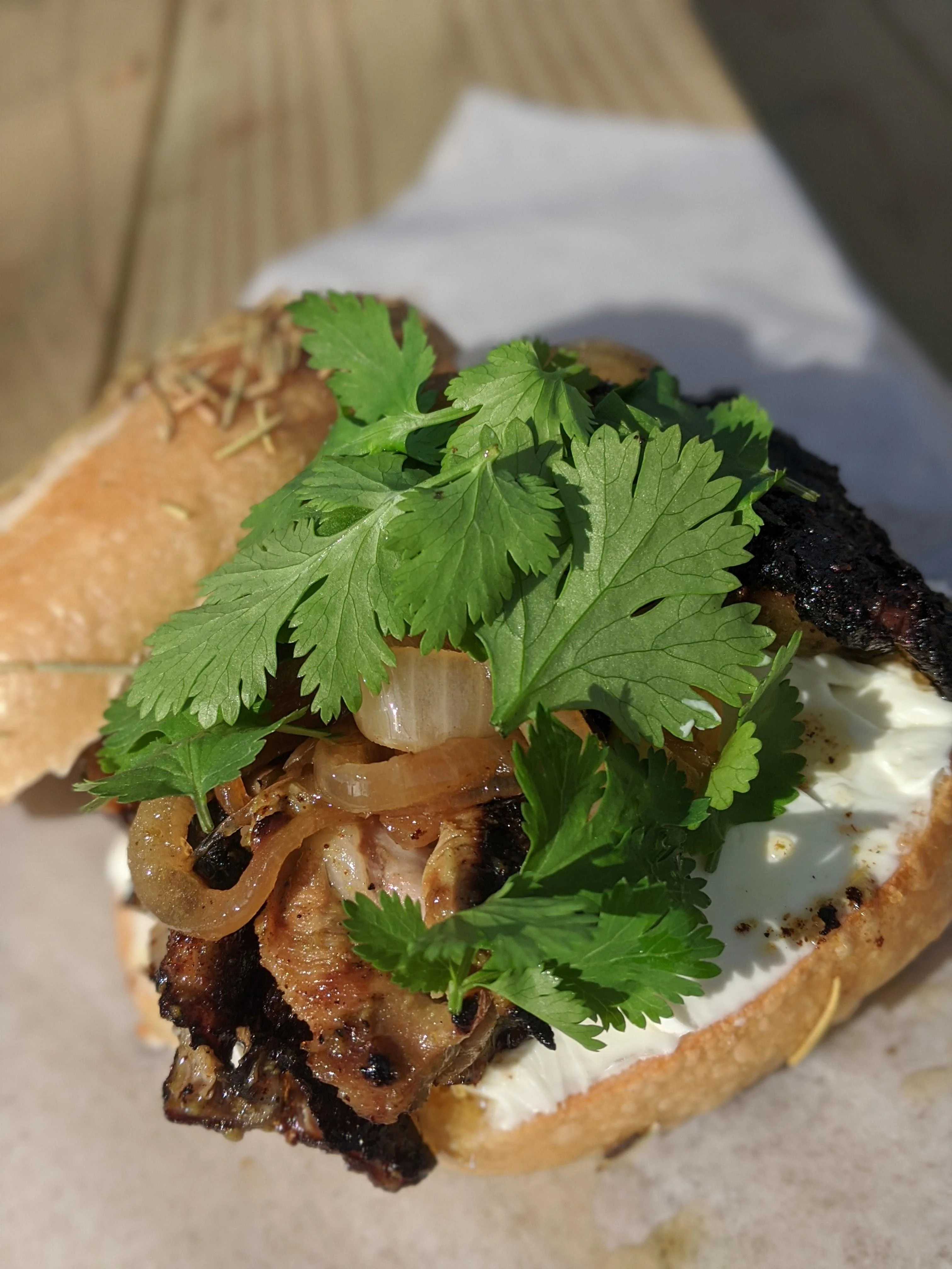 A sandwich featuring grilled meat topped with sautéed onions and fresh cilantro on a bun.
