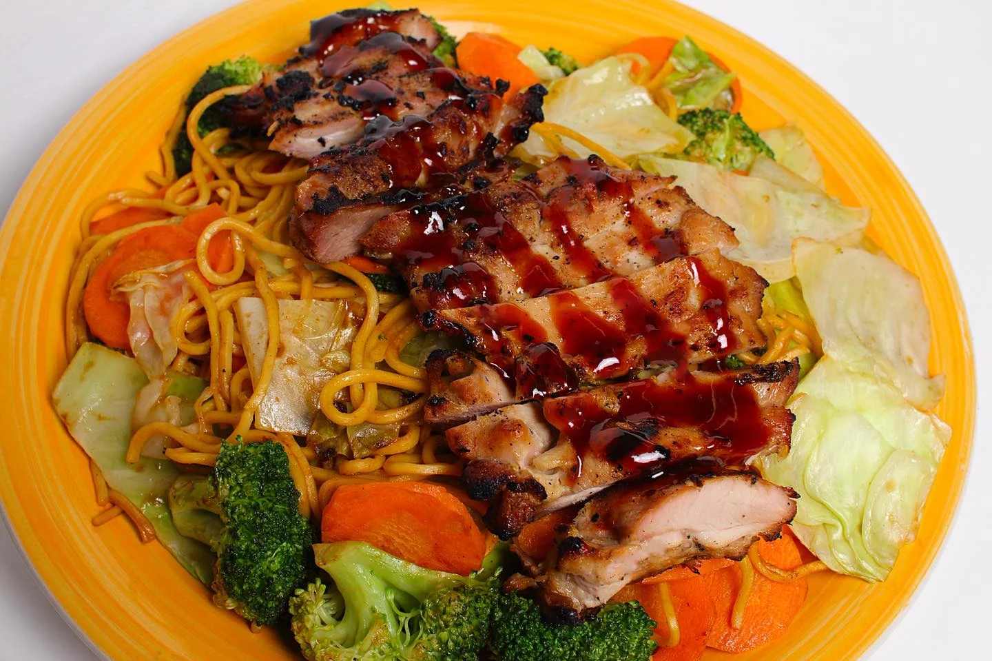 A plate of grilled chicken served on a bed of stir-fried noodles and mixed vegetables, drizzled with sauce.