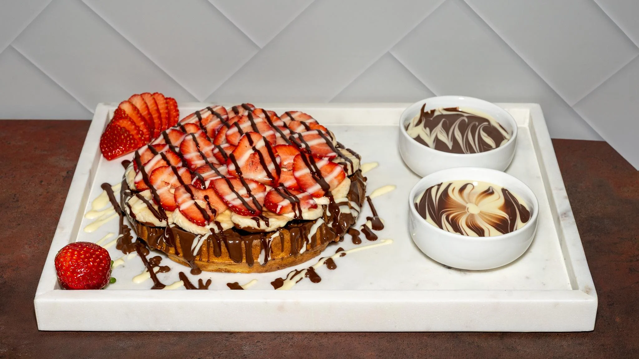 A delicious cake topped with fresh strawberries and chocolate drizzle, served alongside two bowls of chocolate sauce.