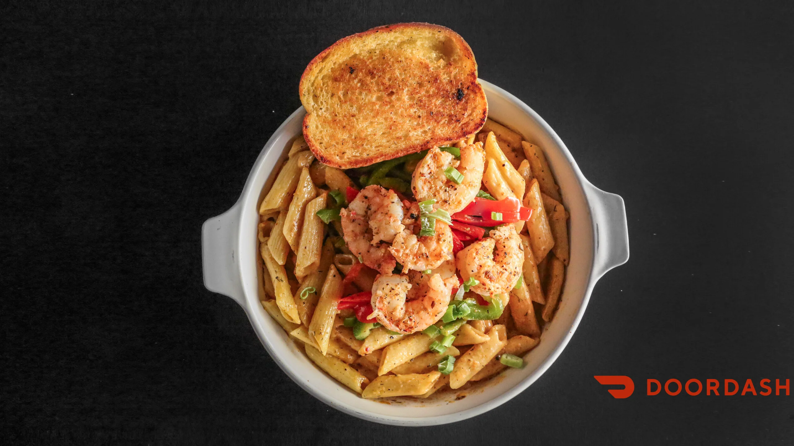 A bowl of creamy pasta with shrimp, bell peppers, and green onions, accompanied by a slice of toasted bread.