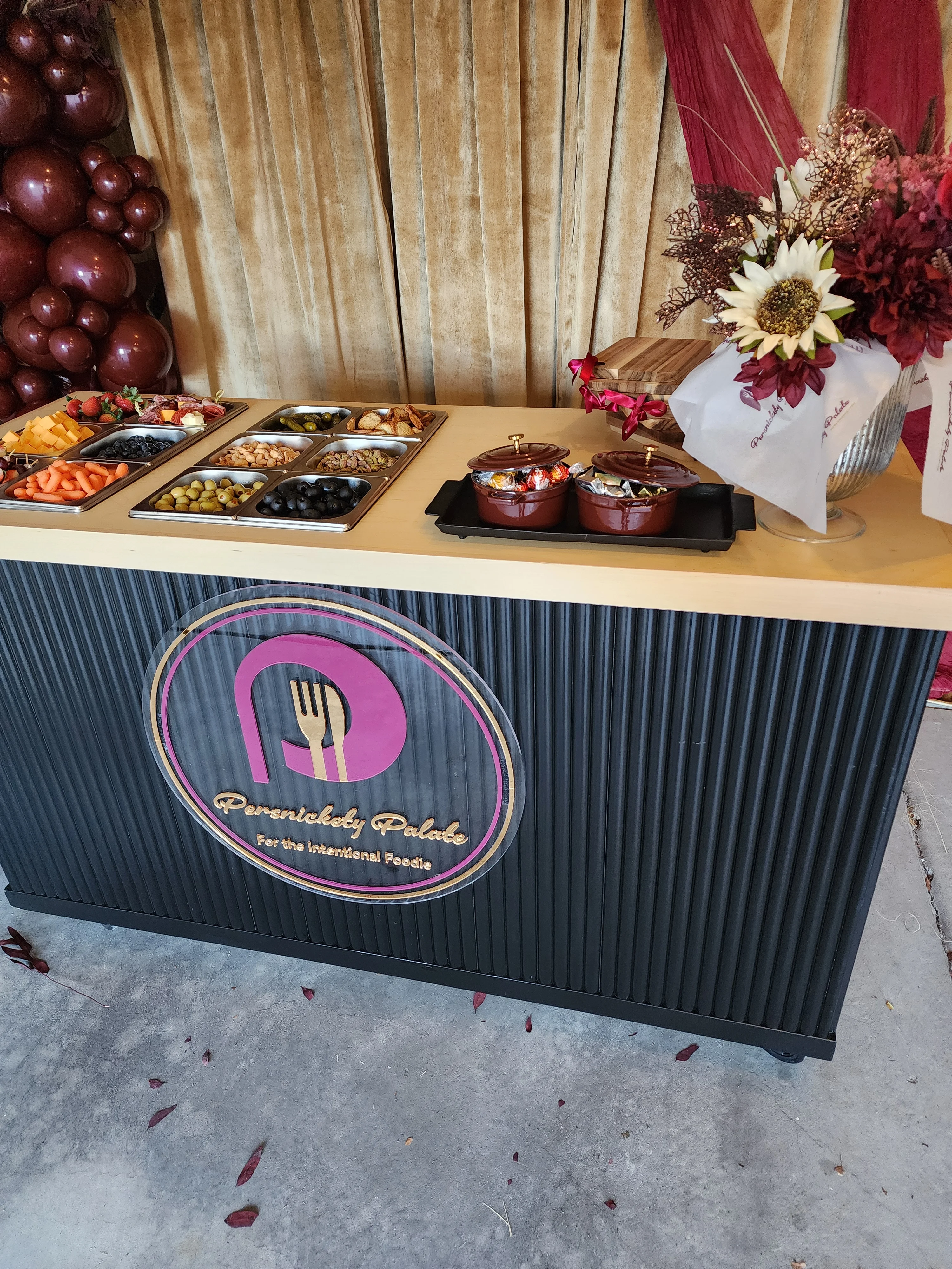 A buffet table showcasing a variety of food options, including fruits, nuts, and snacks, with an elegant floral arrangement to the side.