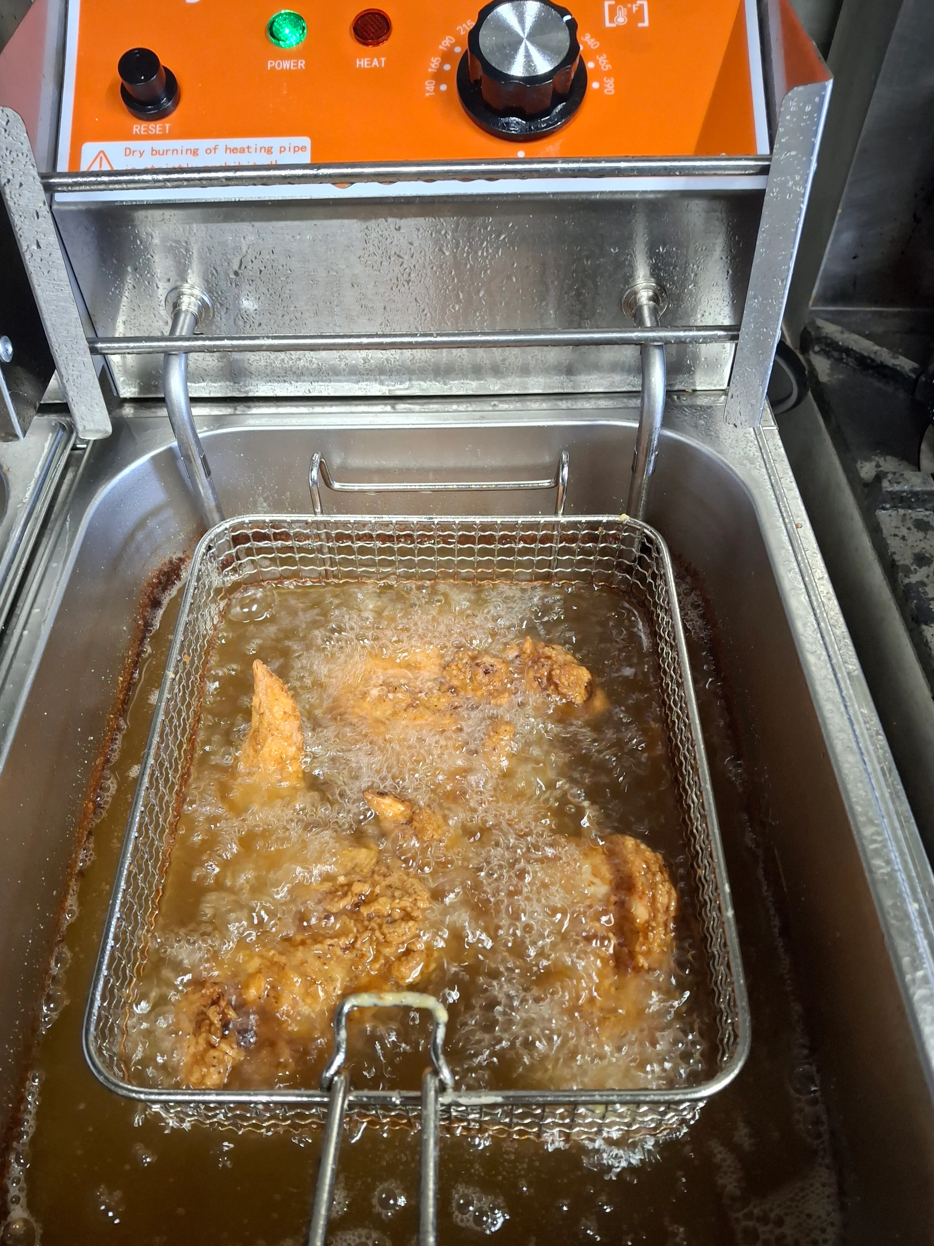 Chicken pieces frying in hot oil inside a deep fryer.