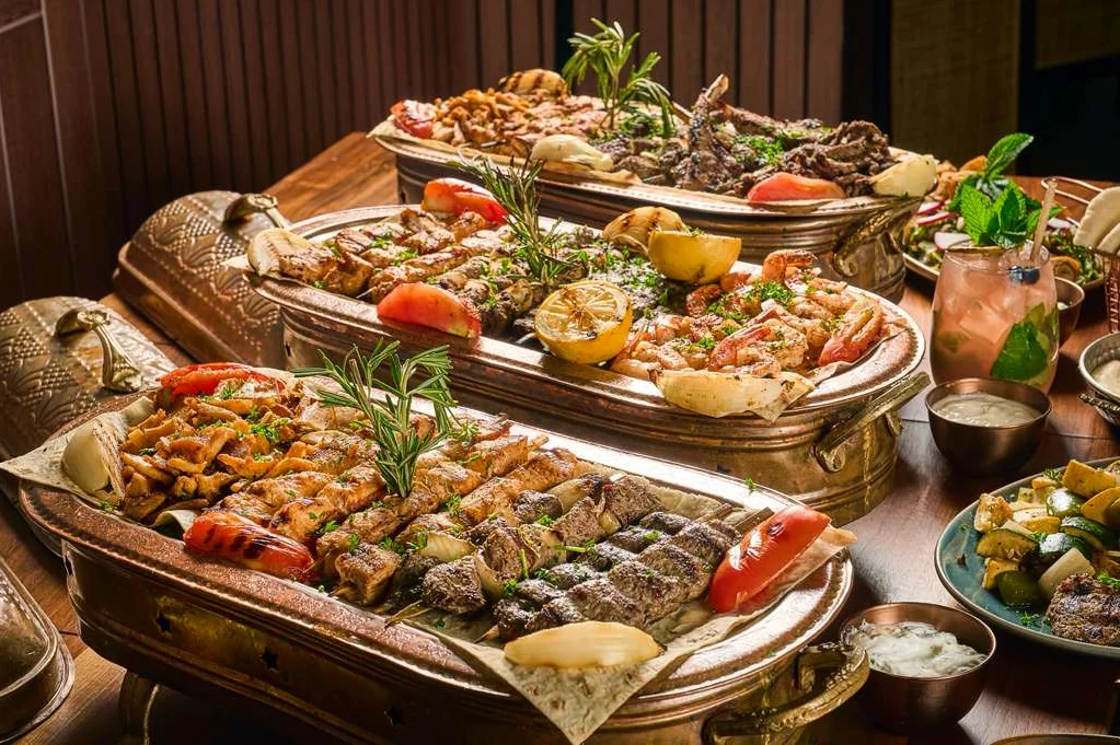 A table filled with Middle Eastern dishes, including hummus, pita, and falafel. Two wine glasses and a beer bottle add a festive touch.