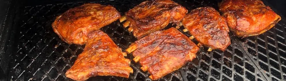 Racks of barbecue ribs cooking on a grill, coated in smoky sauce and charred to perfection.