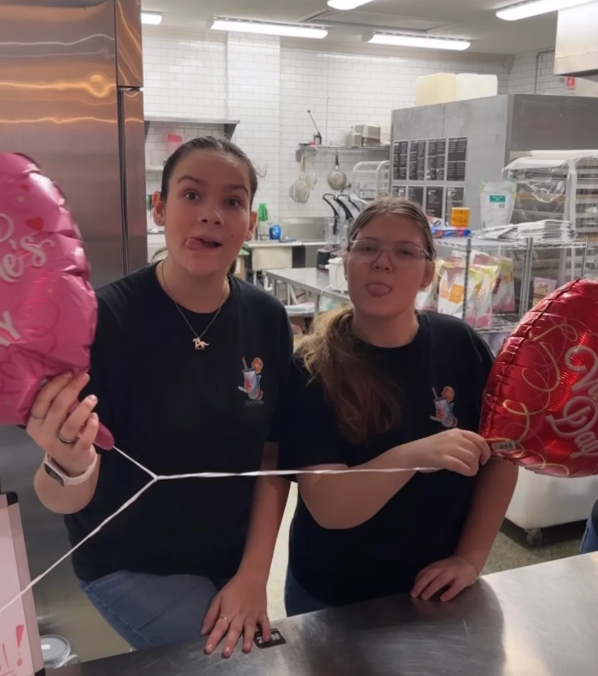 Two staff members celebrating with balloons in a restaurant kitchen