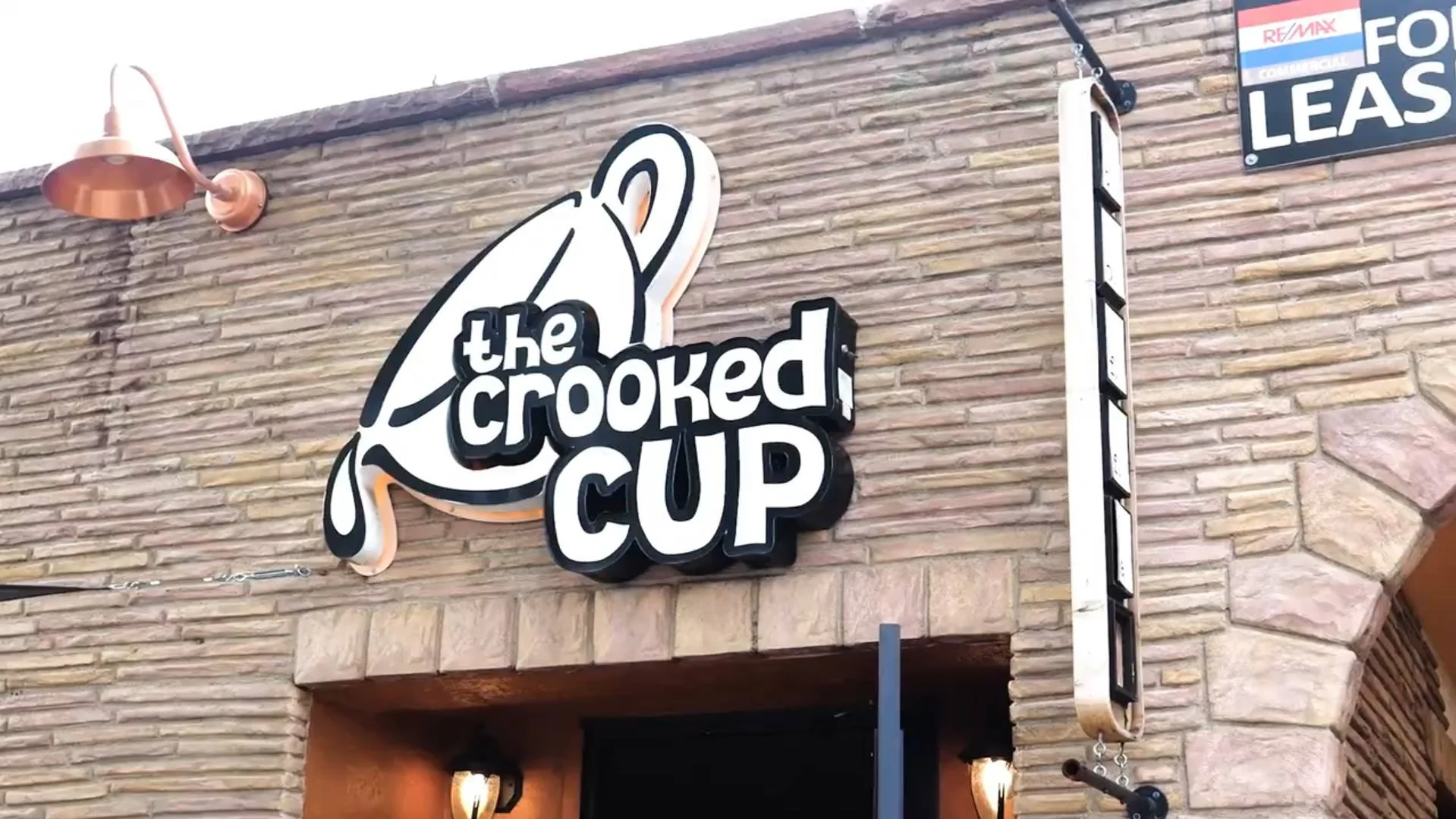 Signage of The Crooked Cup coffee shop with rustic stone wall