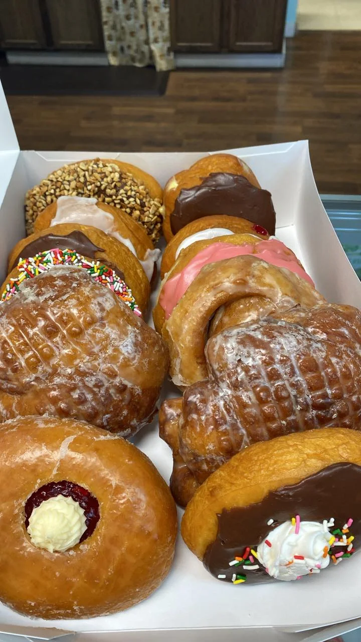 A diverse assortment of donuts in a box, featuring various toppings like sprinkles, chocolate, and cream filling.