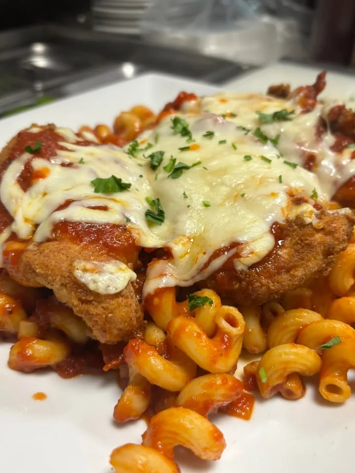 A delicious plate of baked chicken over spiral pasta, topped with marinara sauce and melted cheese, garnished with herbs.