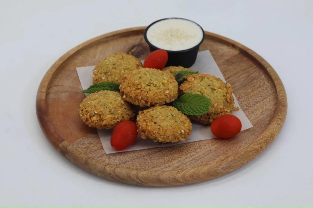 A plate of falafel balls served with cherry tomatoes and a small cup of dipping sauce.
