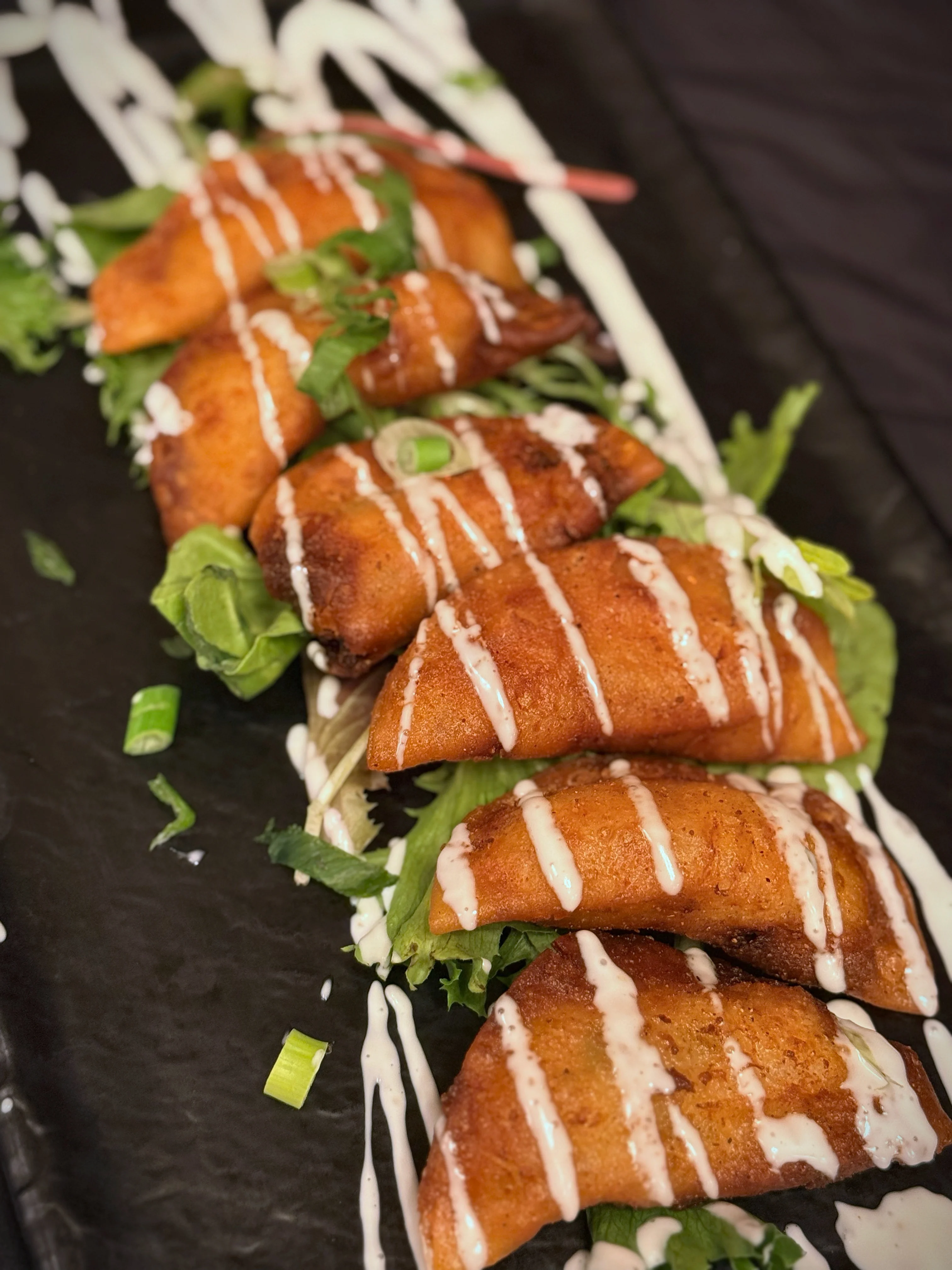 A platter of golden-brown fried snacks drizzled with a creamy sauce and garnished with fresh greens.