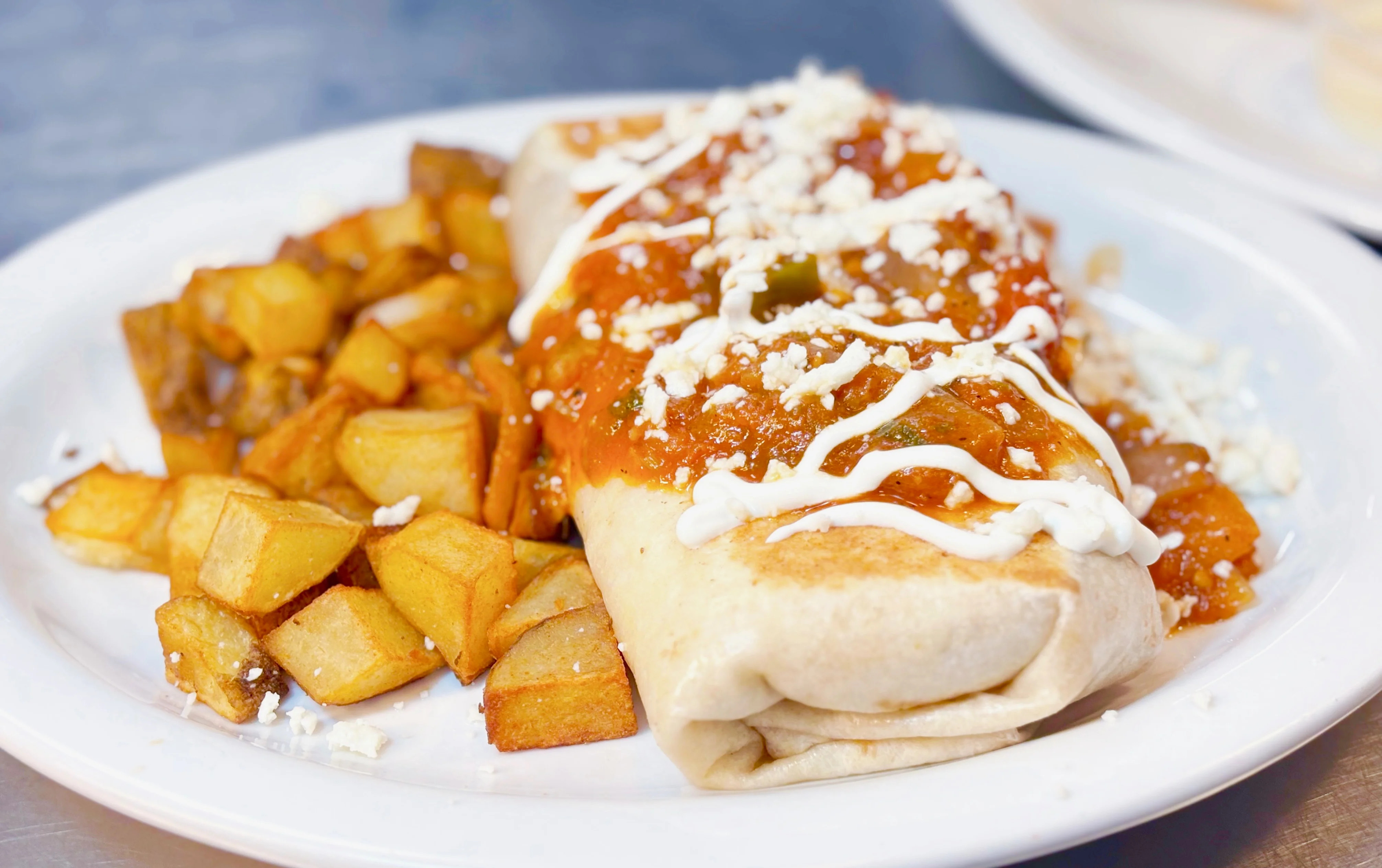 Delicious Mexican burrito topped with sauce and served with crispy potatoes