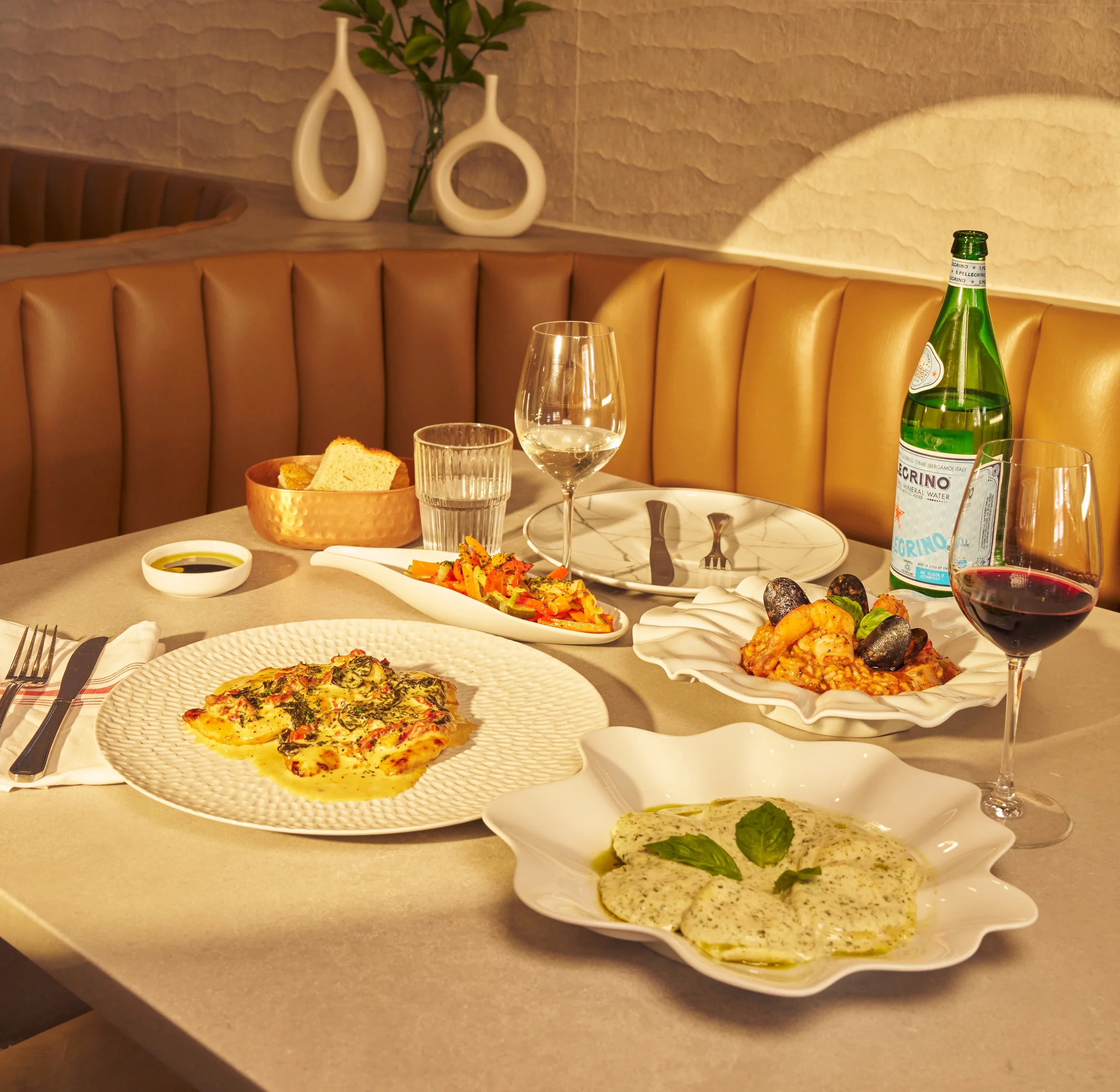 A spread of food from Five Corners Ristorante including: creamy tuscan chicken, seafood risotto, fresh focaccia, and red wine