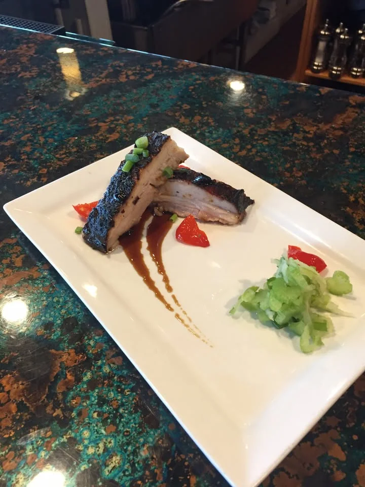 A plated dish featuring a piece of grilled meat with garnishes and sauces, served on a decorative plate.