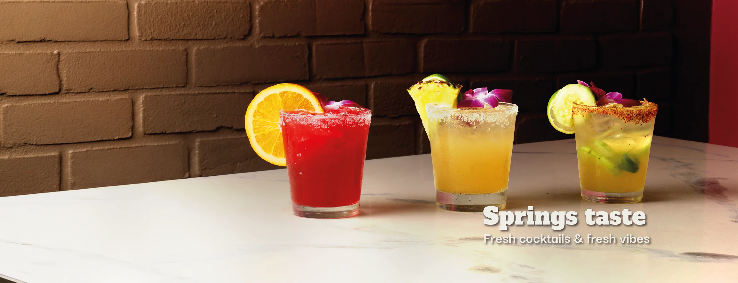 Three colorful cocktails with fresh ingredients on a marble table.