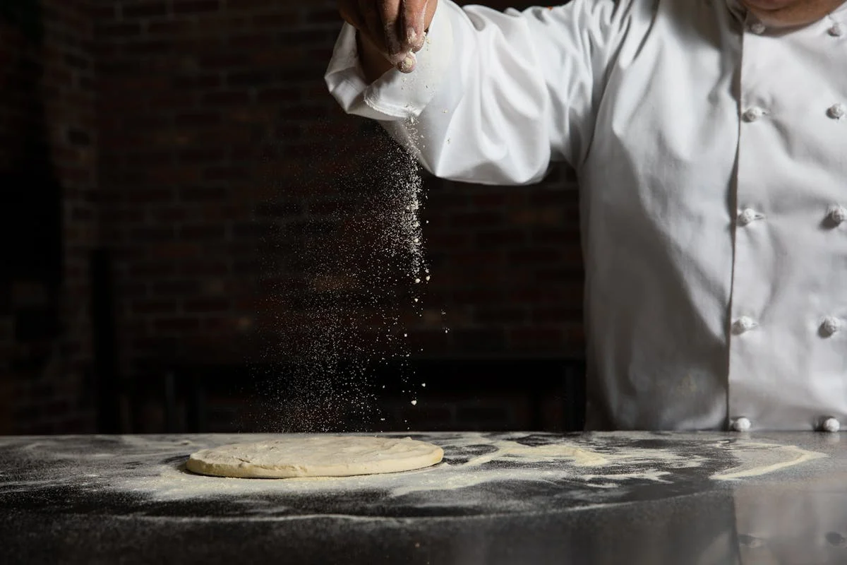 A chef sprinkling flour on dough
