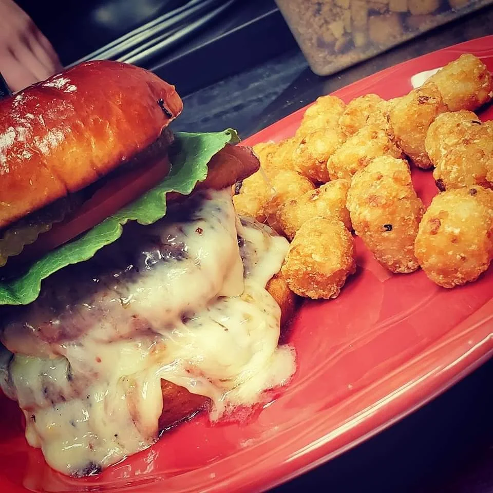 Juicy cheeseburger with tater tots on a red plate
