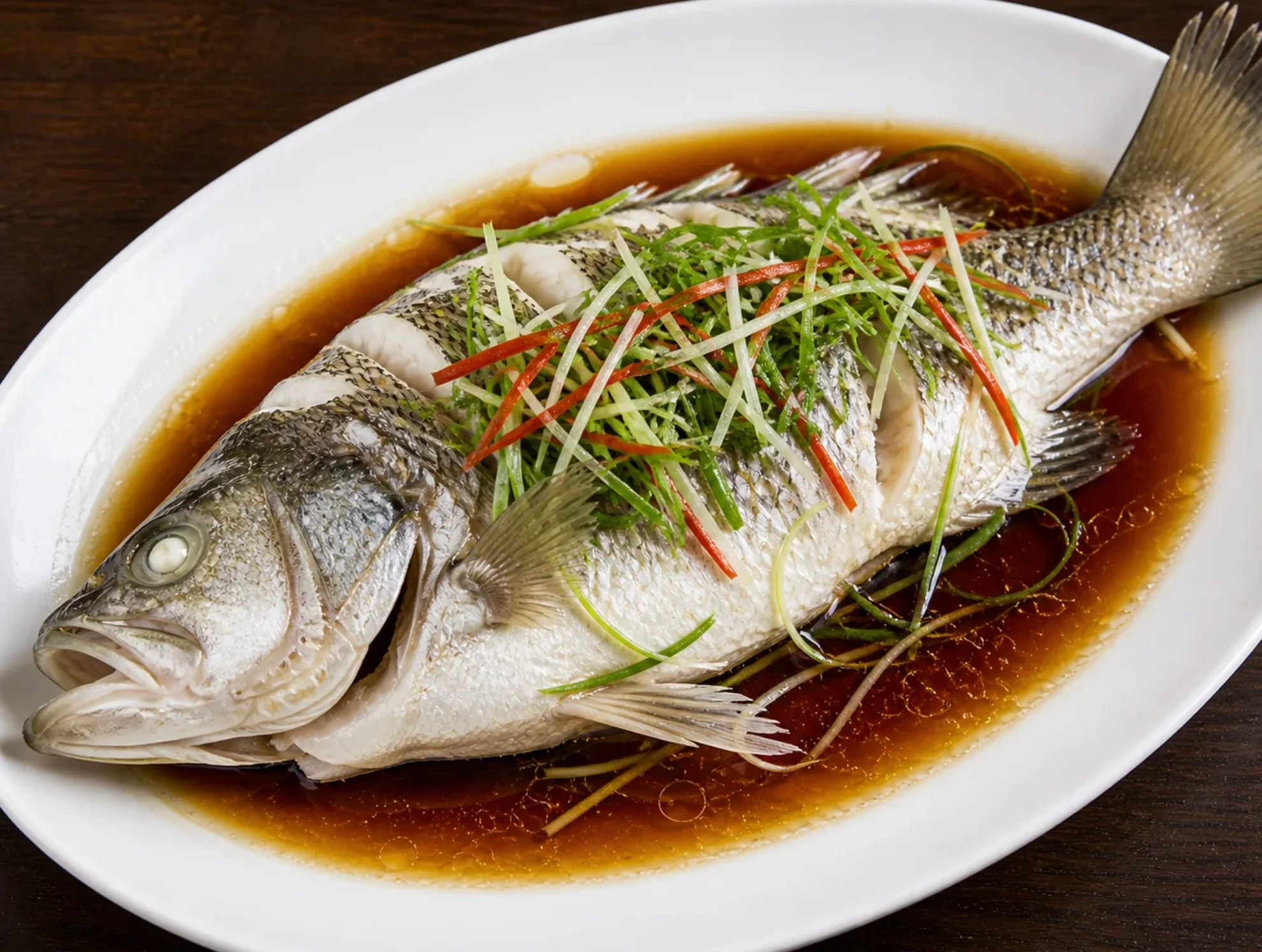 Steamed fish garnished with green onions and red peppers in soy sauce.