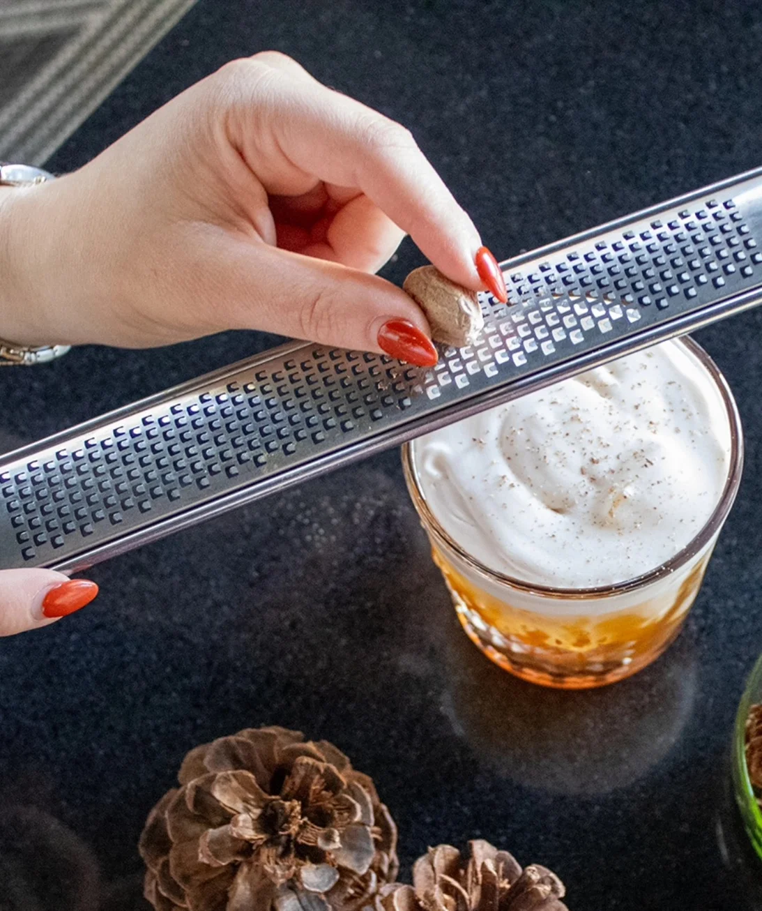 Bartender grating nutmeg over a cocktail with frothy cream