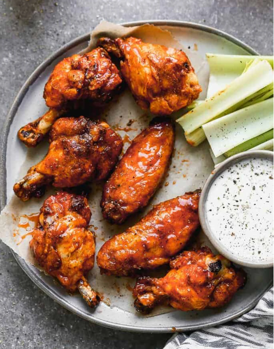 A plate of spicy chicken wings served with celery sticks and a side of ranch dipping sauce.