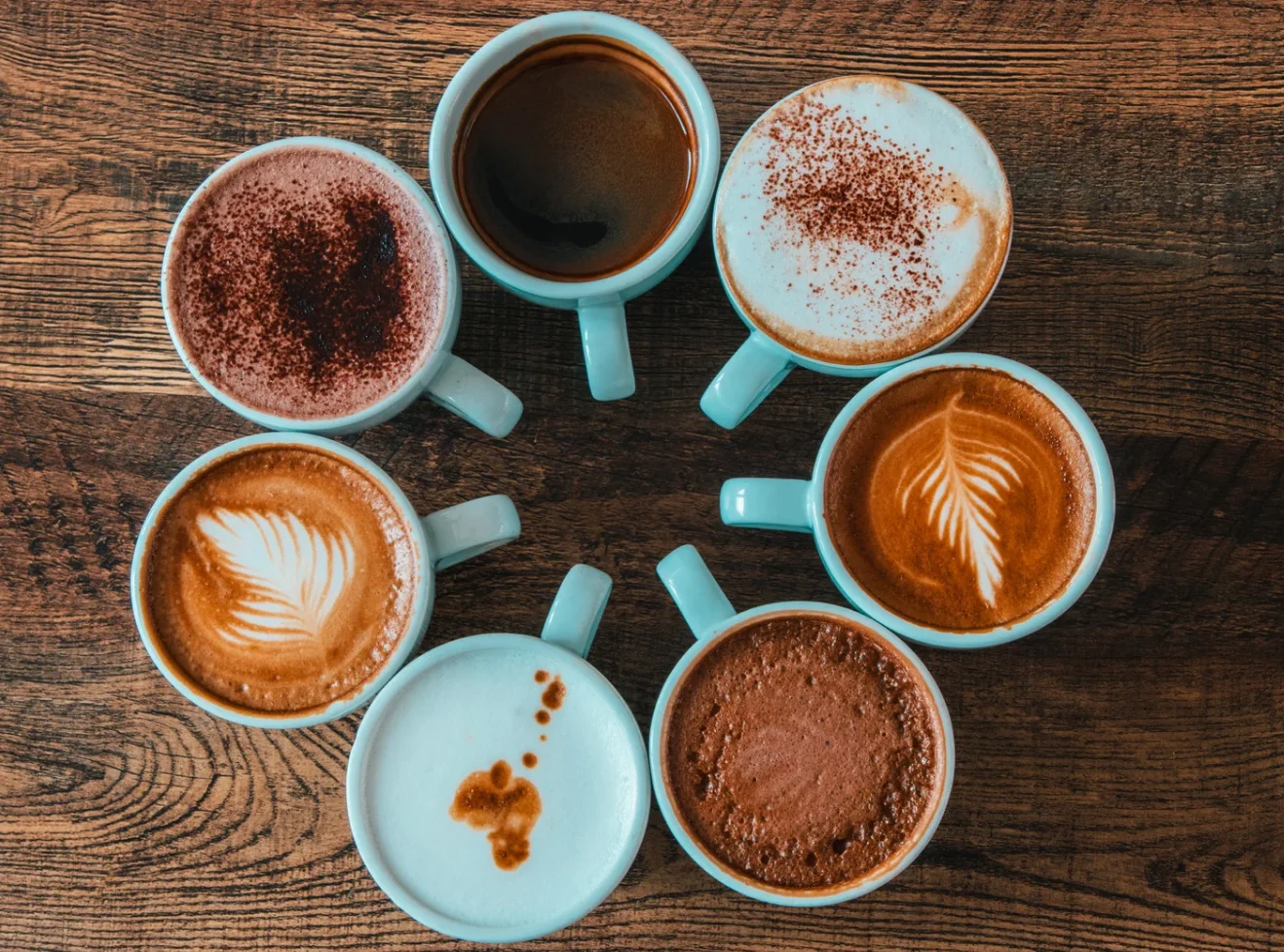 Variety of coffee styles in white ceramic mugs and presentations over a wood table 