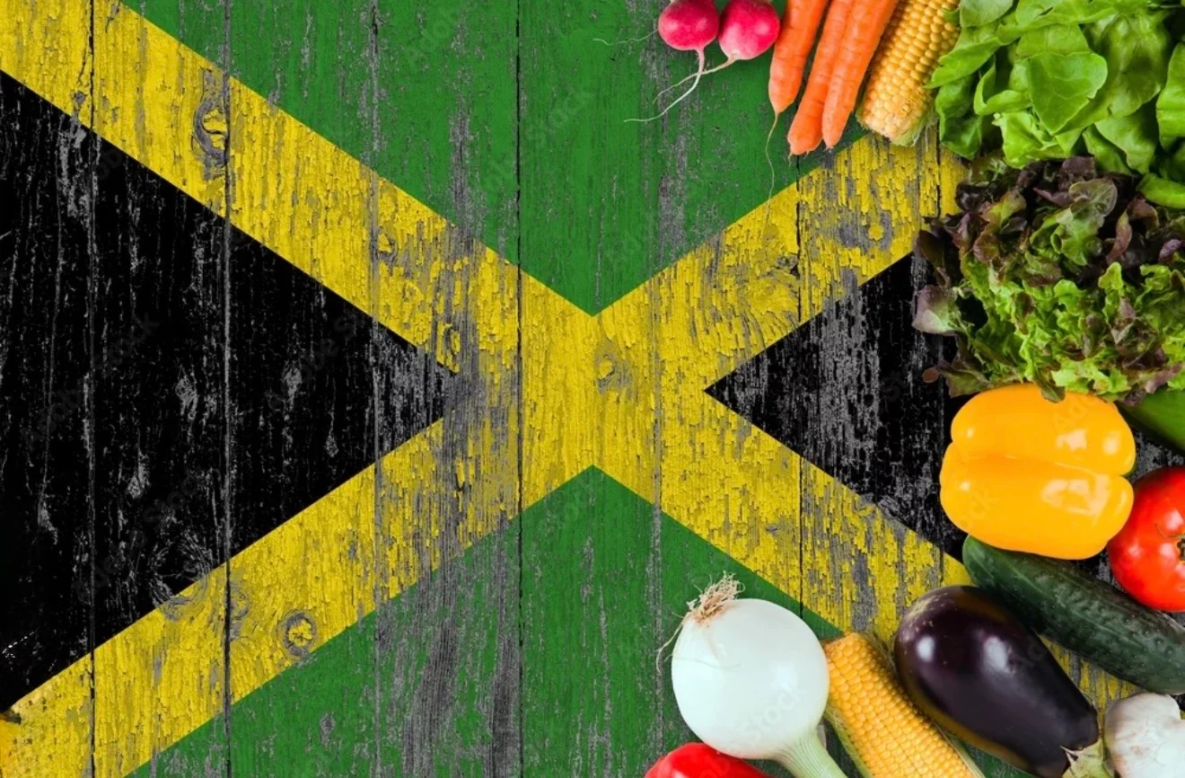 A rustic wooden background featuring the Jamaican flag, surrounded by fresh vegetables like carrots, lettuce, and peppers.