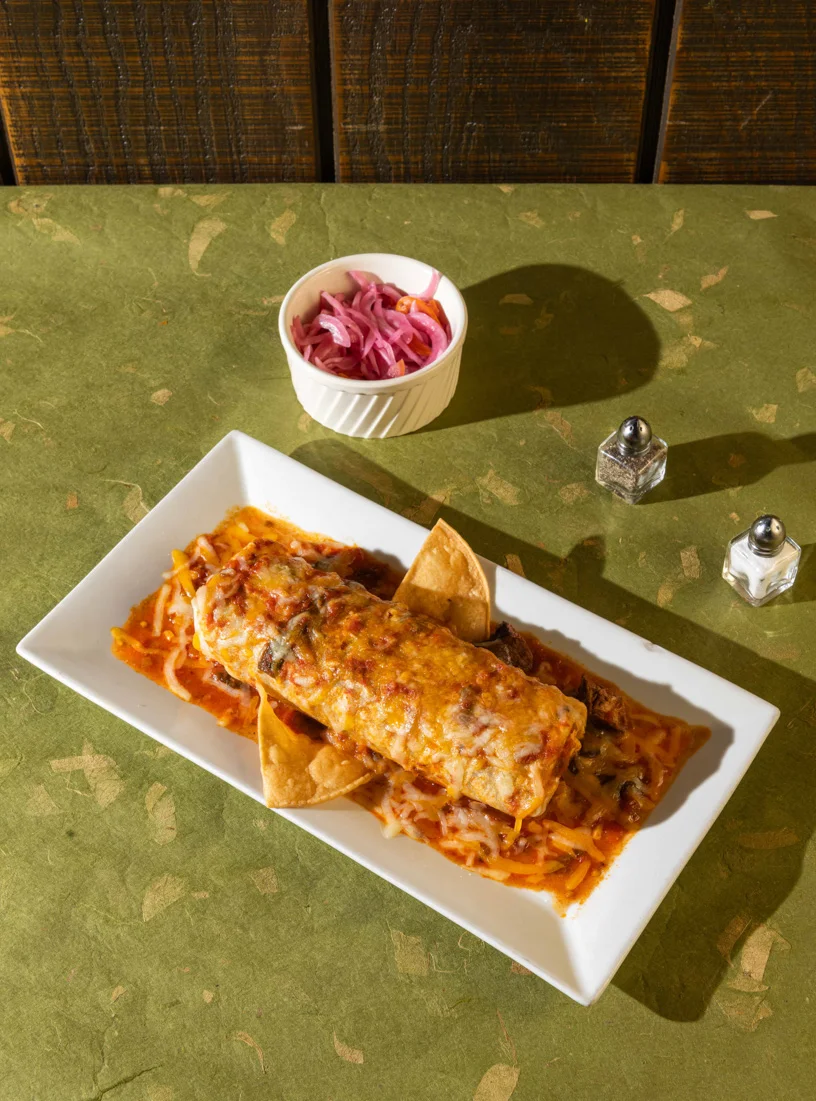 Cheesy baked burrito topped with red sauce, served with tortilla chips and a side of pickled onions at Friducha in Brooklyn, NY.