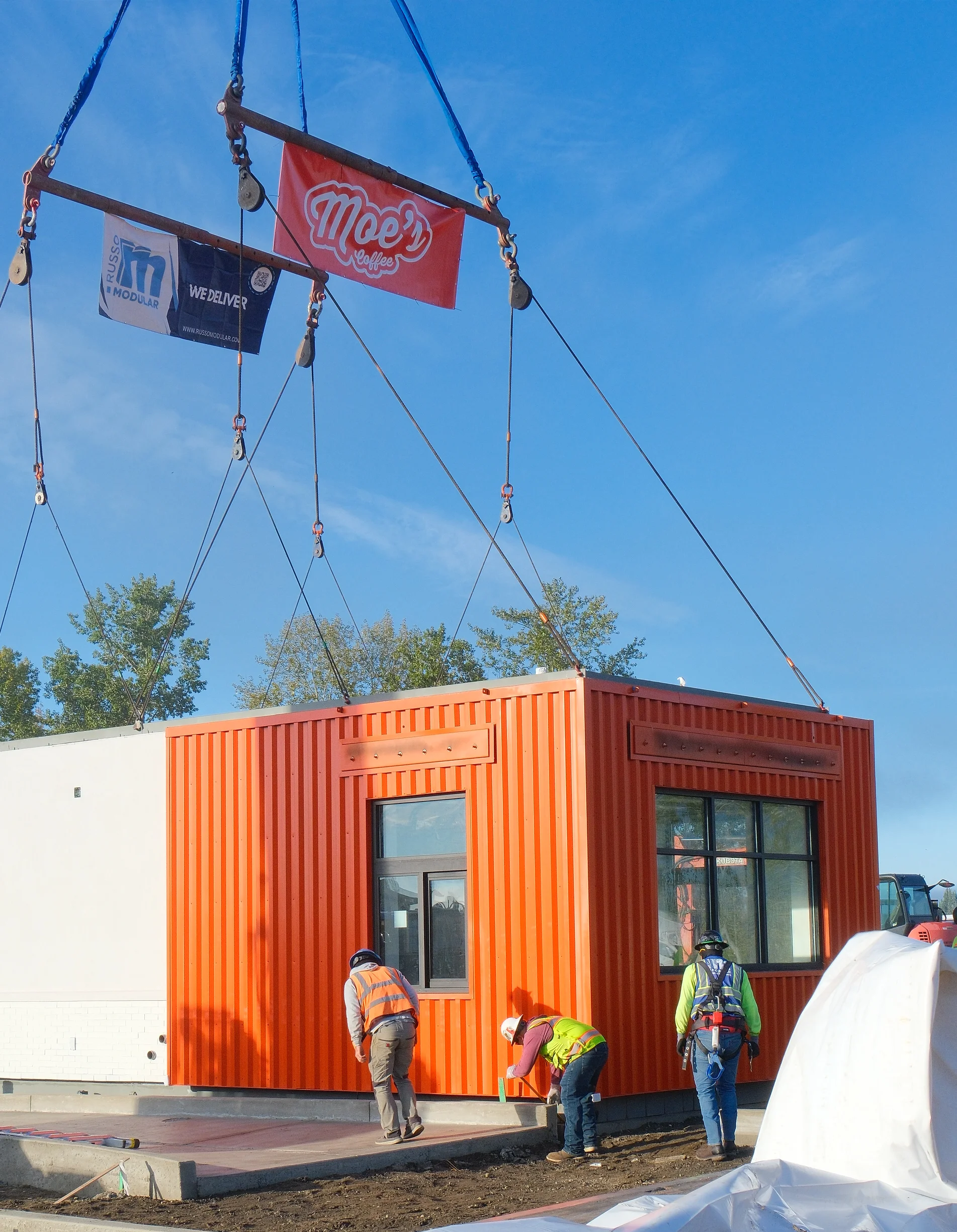 Orange container restaurant under construction with workers and hanging coffee signage