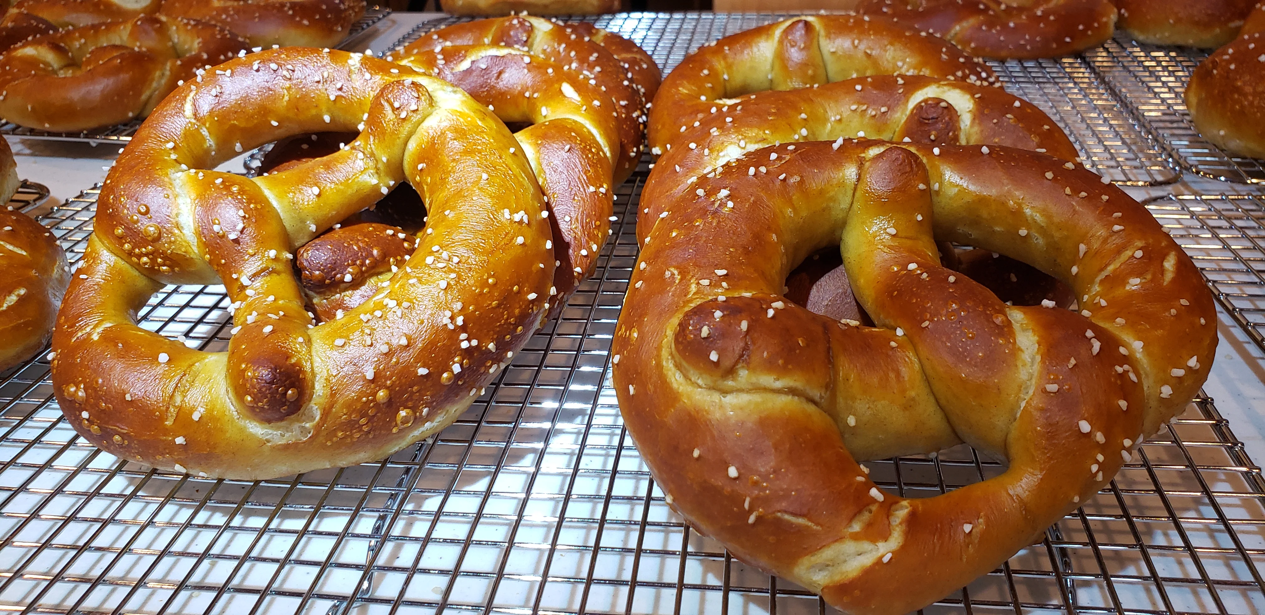 Freshly baked pretzels on a cooling rack, sprinkled with salt.