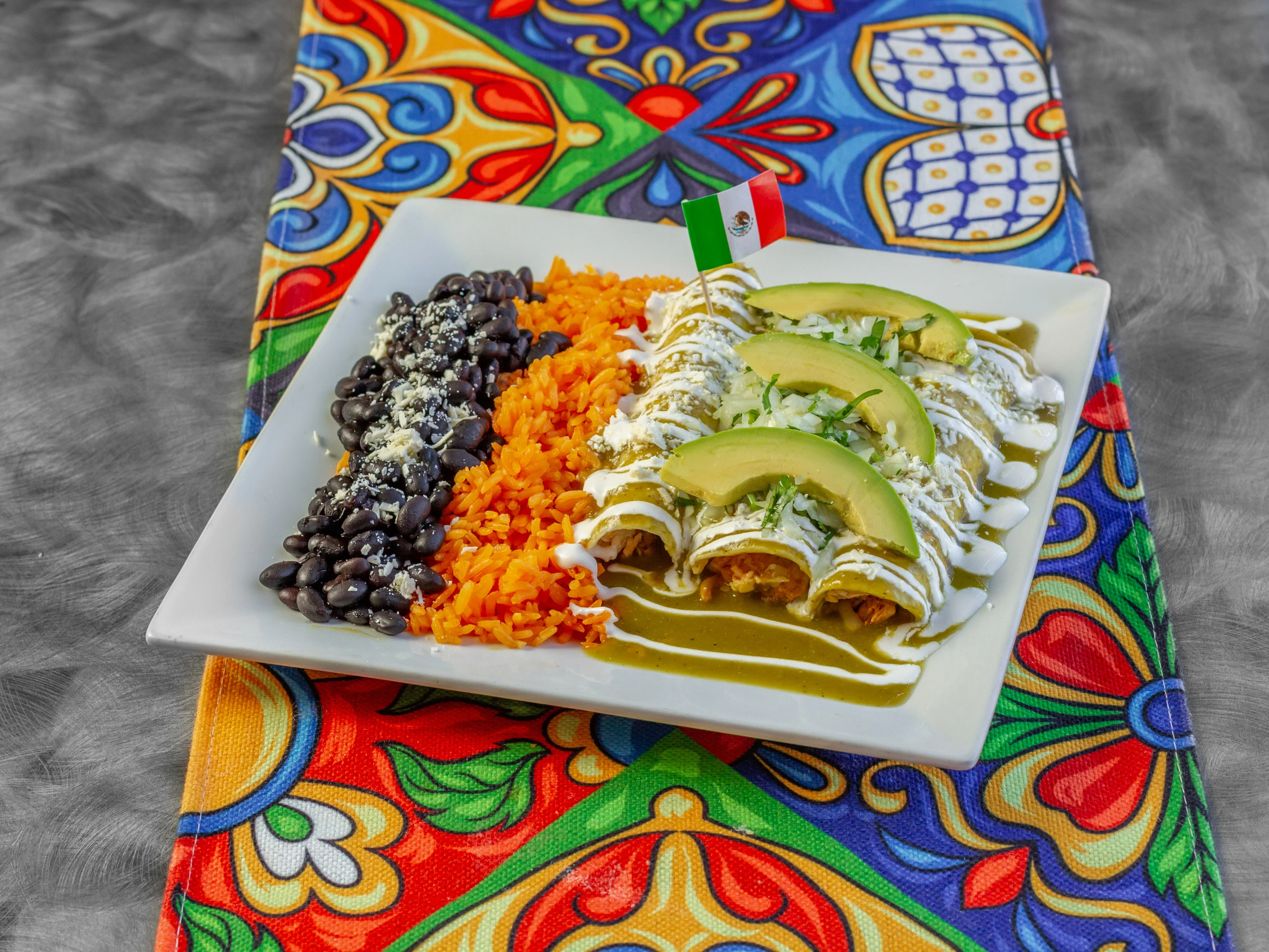 Delicious churros arranged on a white plate, sprinkled with sugar and drizzled with chocolate sauce. The plate is placed on a vibrant, patterned tablecloth.