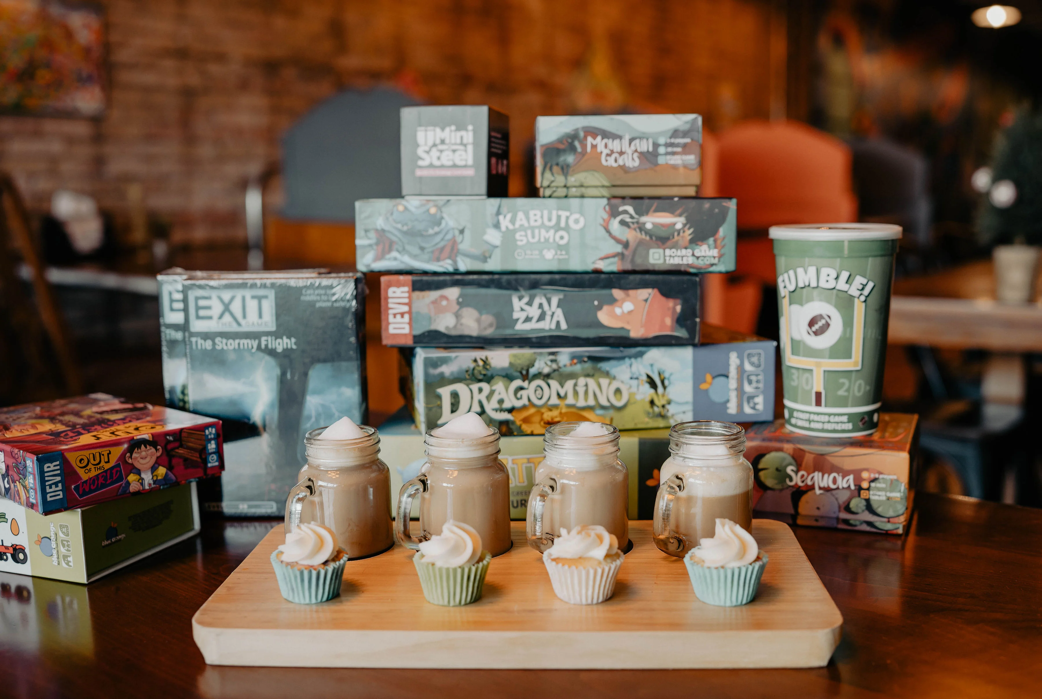 Assorted board games with coffee and cupcakes on a wooden table