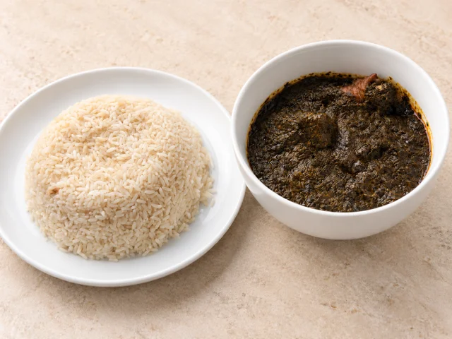A serving of white rice shaped into a mound alongside a bowl of dark green sauce with pieces of meat, emphasizing a hearty meal.