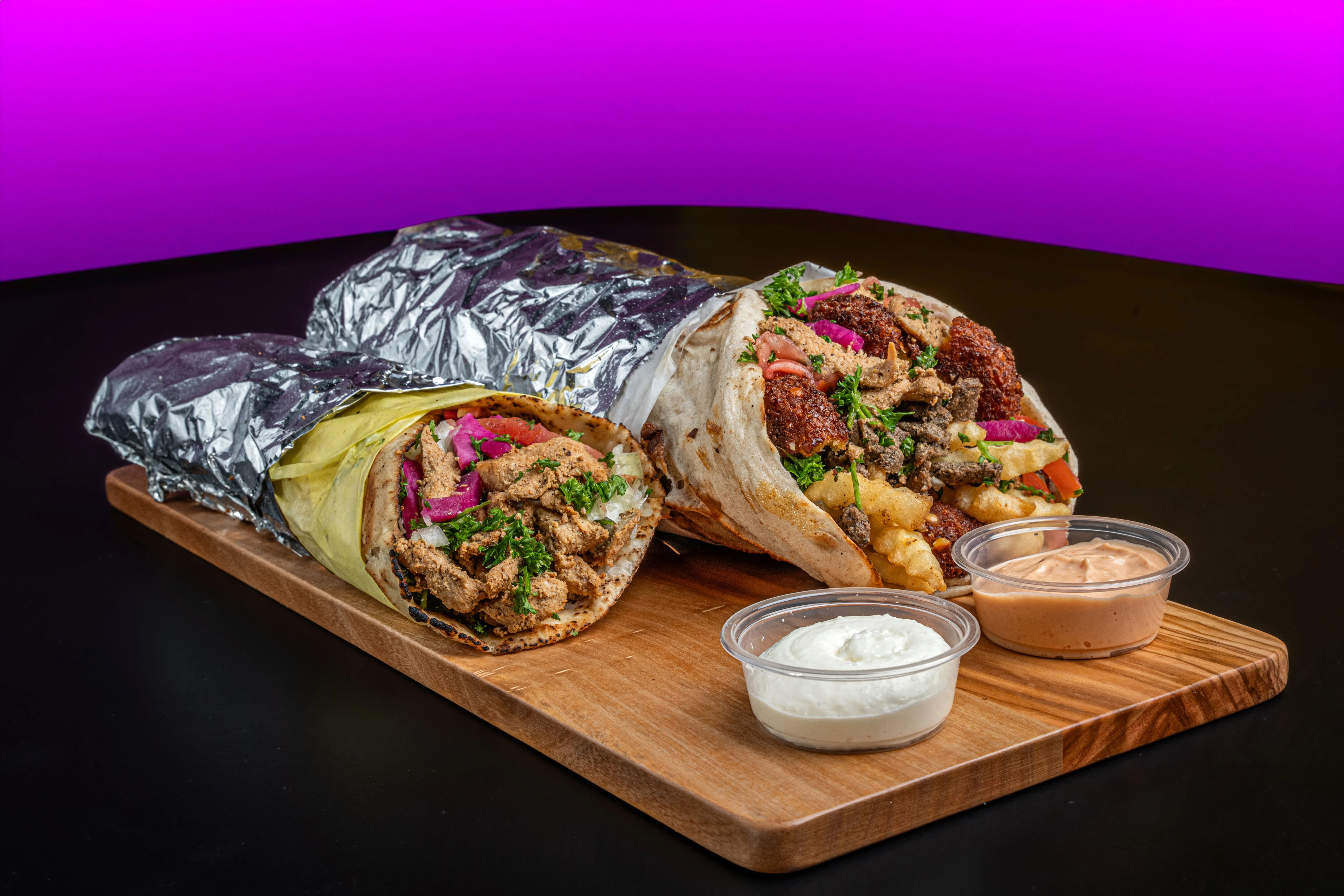 Two delicious wraps with fillings and sauces on a wooden board.