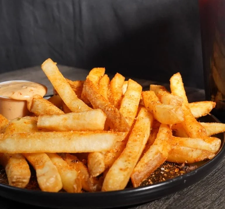 A plate of golden French fries seasoned and served with a creamy dipping sauce.