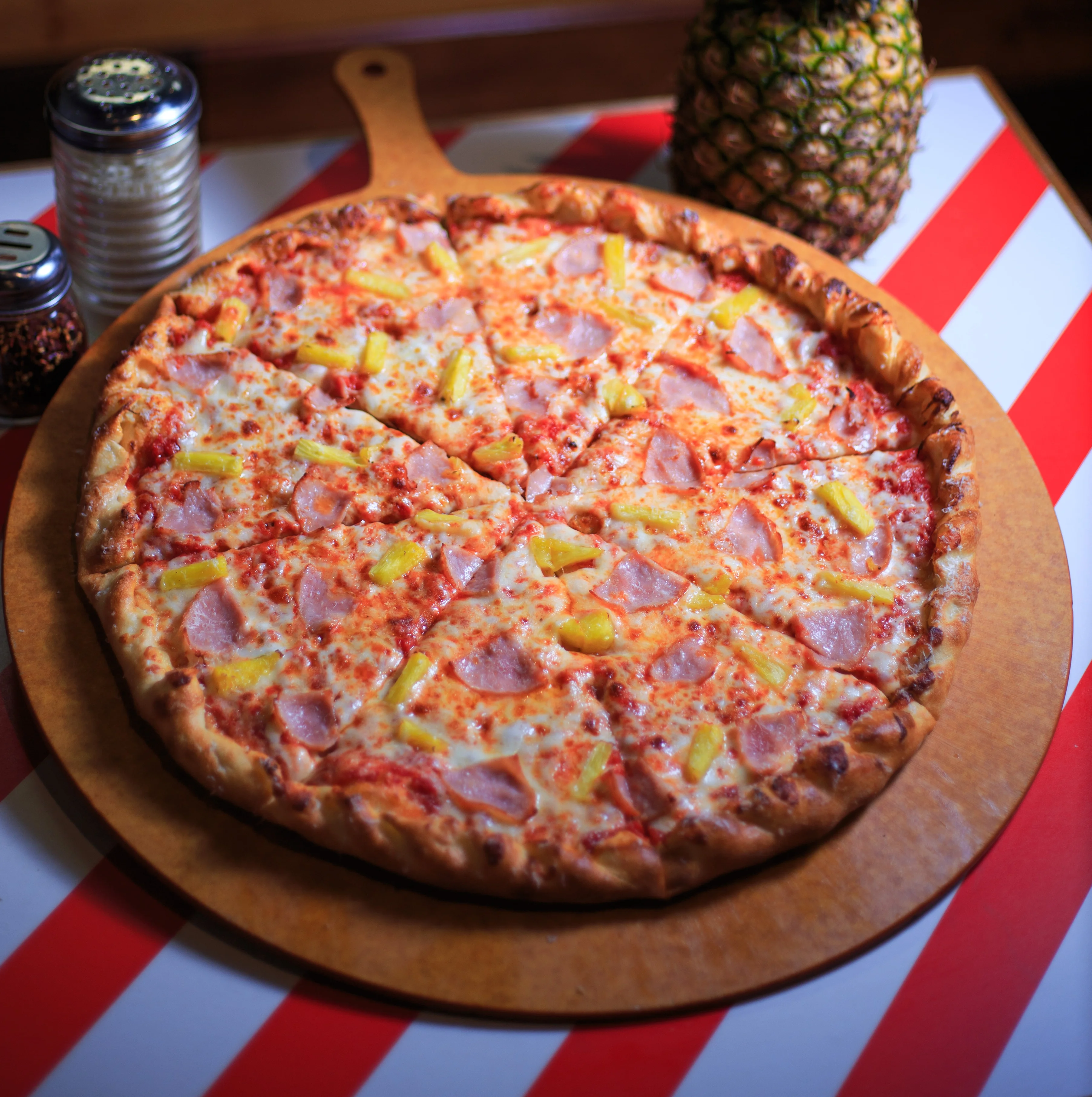 Hawaiian pizza with ham and pineapple on a wooden serving board
