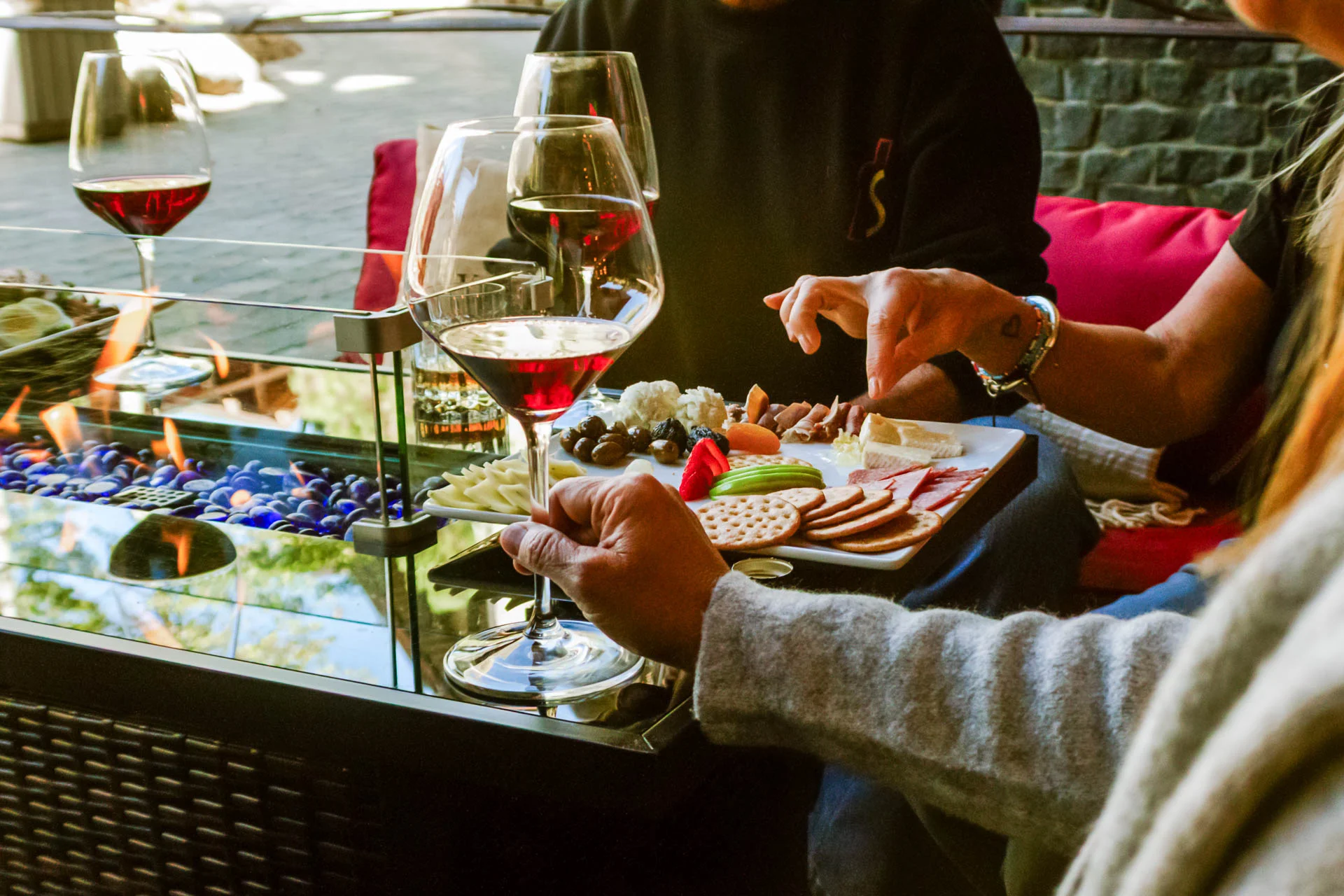 Cozy outdoor scene at Side Door Wine Bar & Café with wine glasses by a glowing fireplace, inviting visitors to get in touch.