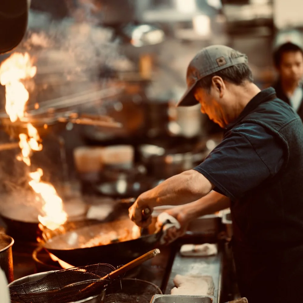 Chef stir-frying in a busy Asian kitchen with flames