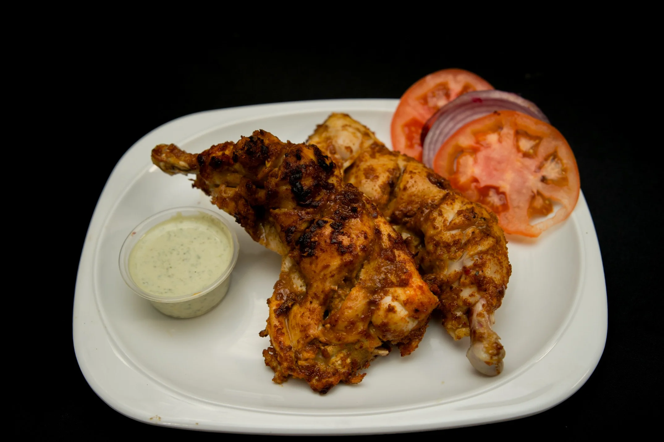 Grilled chicken Bihari tikka served with creamy herb sauce and fresh tomato and onion garnish at Karachi BBQ Tonight.