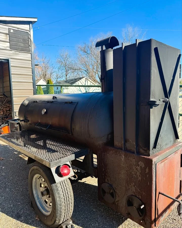 A black barbecue smoker on a trailer, ready for outdoor cooking, with a clear blue sky in the background.