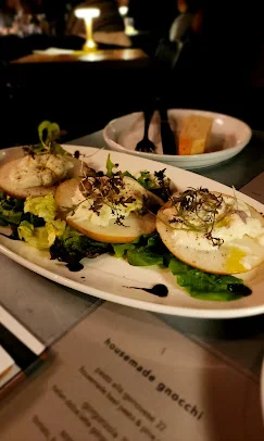 Three plates of gnocchi are served on a bed of greens, garnished with microgreens and a drizzle of sauce.