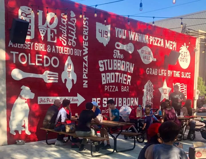 Outdoor dining area at Stubborn Brother Pizza Bar with vibrant mural
