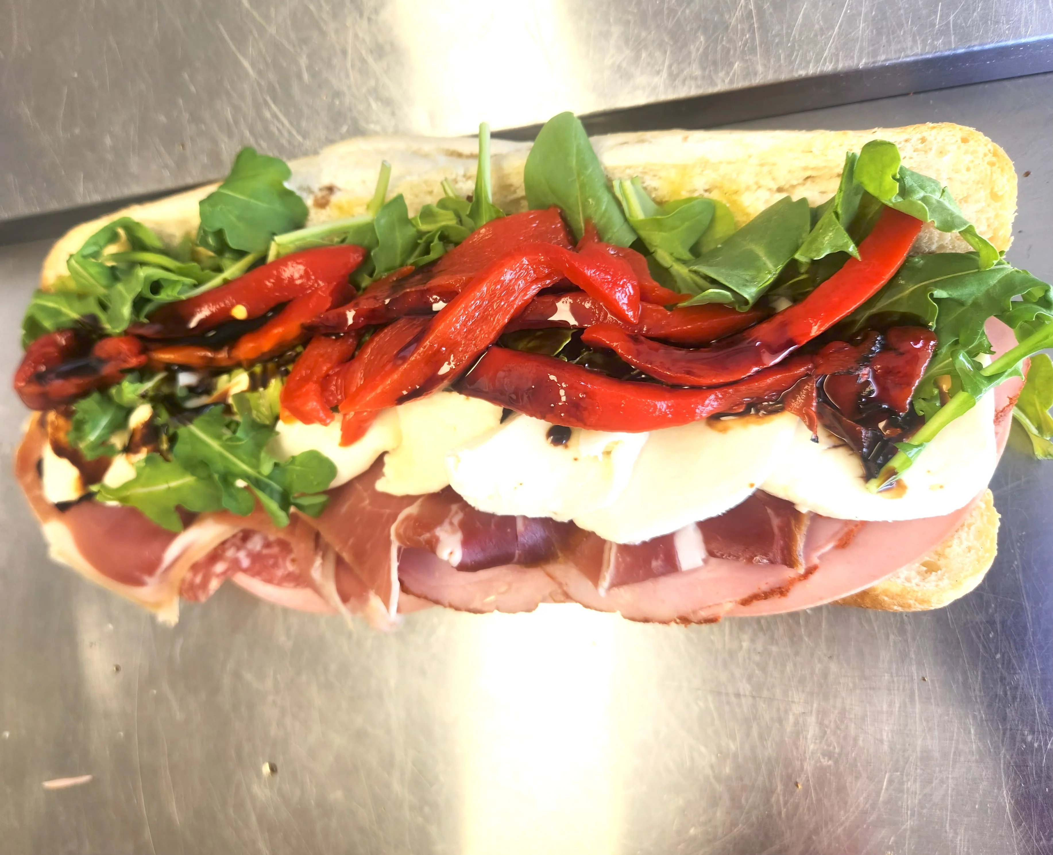 A sandwich filled with cured meats, fresh mozzarella, red peppers, and arugula on a crusty bread.