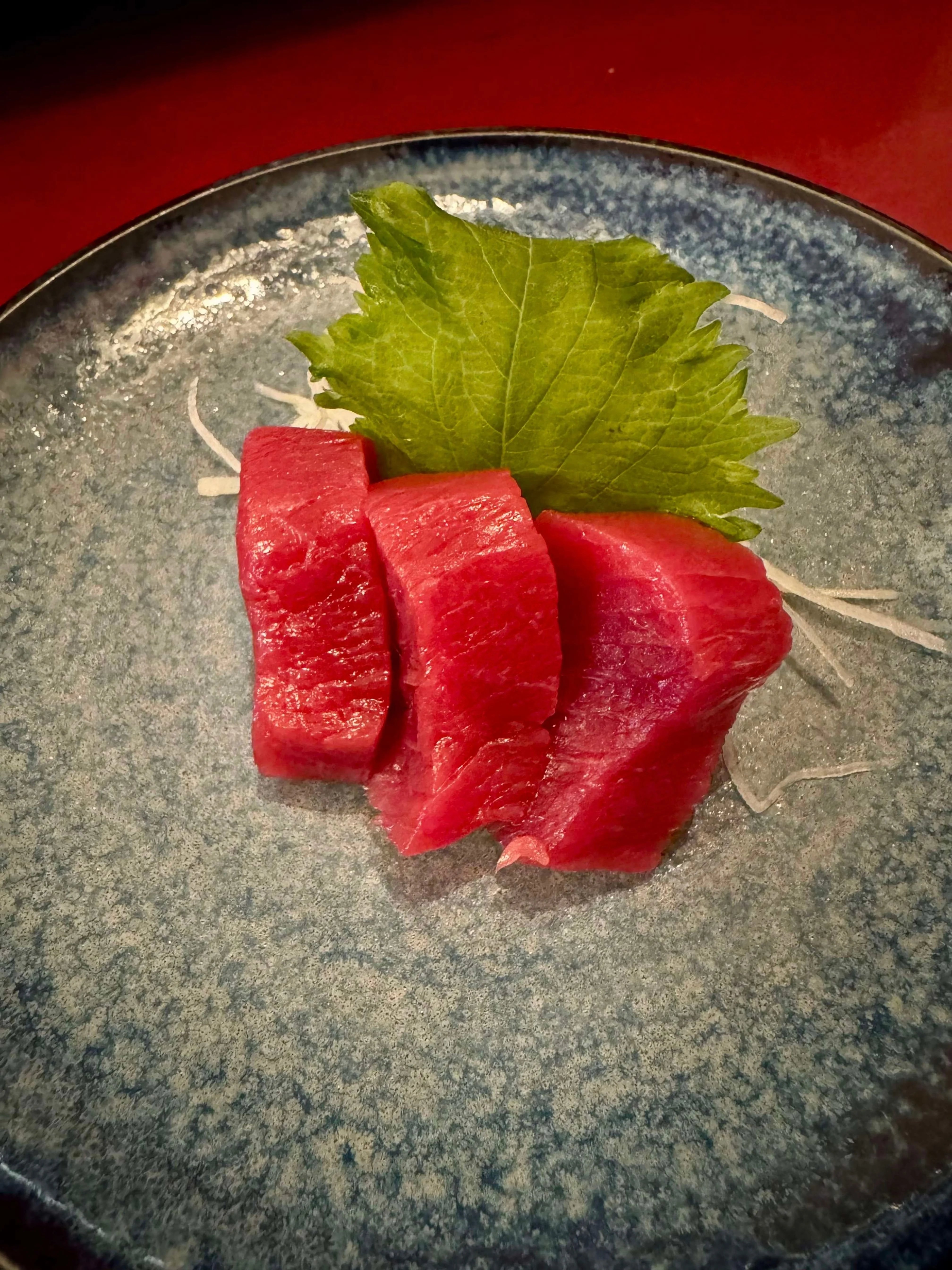 Sashimi-style tuna slices garnished with shiso leaf on a blue plate