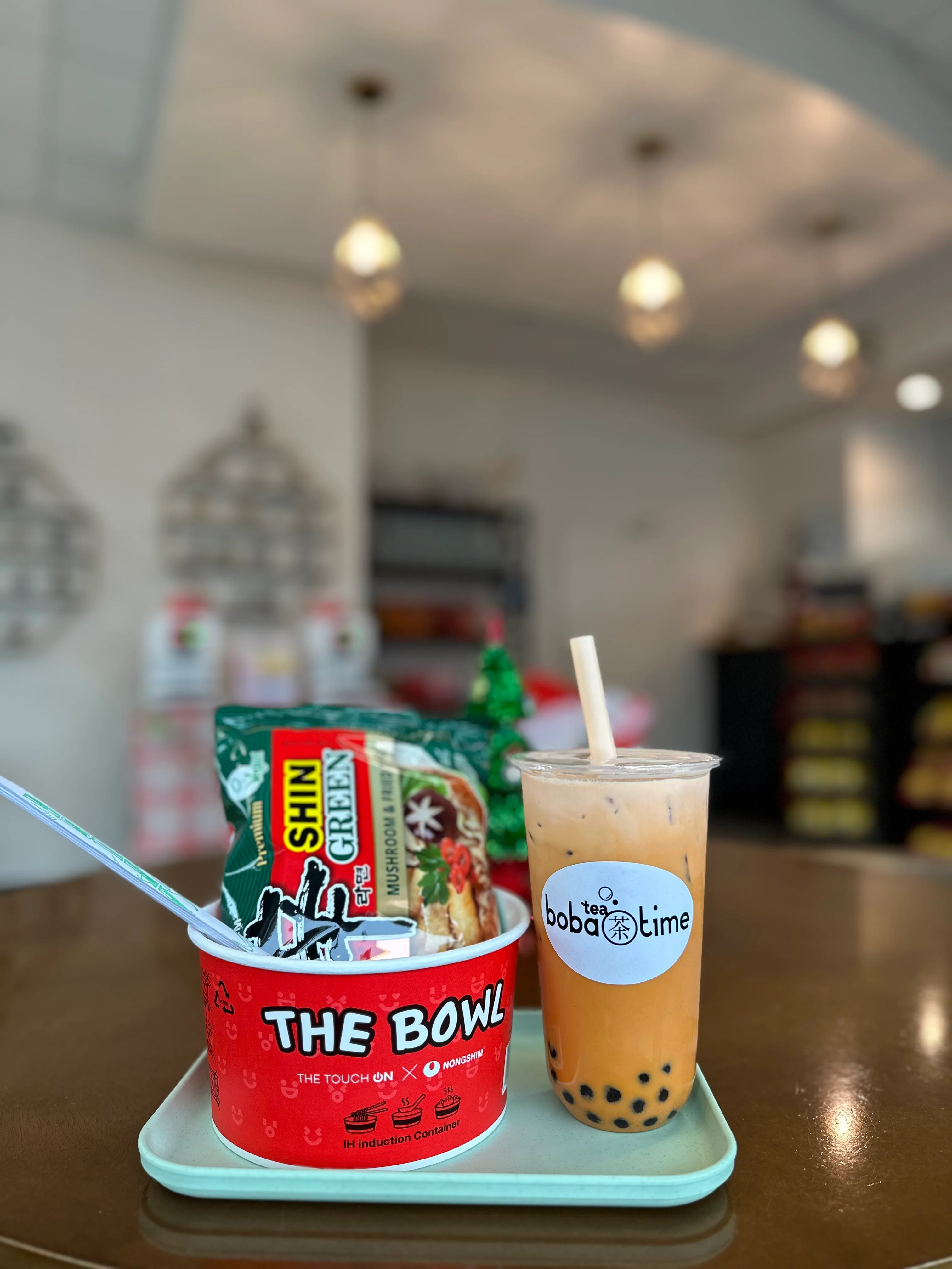 A hand holding a cup of boba tea with a purple straw. The cup features a label with the brand name and a decorative background.